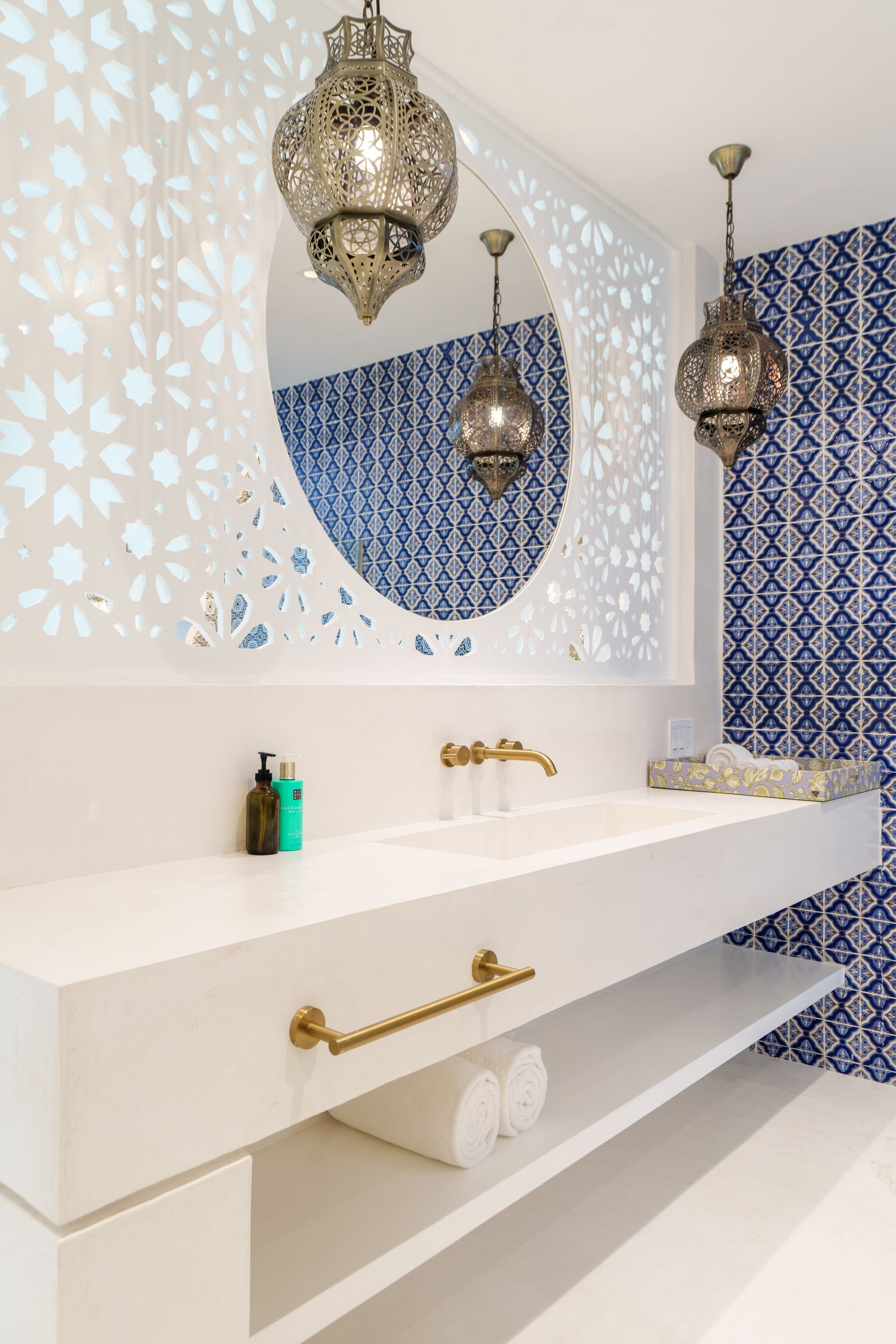 Bathroom with white vanity, blue patterned tile, gold fixtures, and ornate pendant lights.