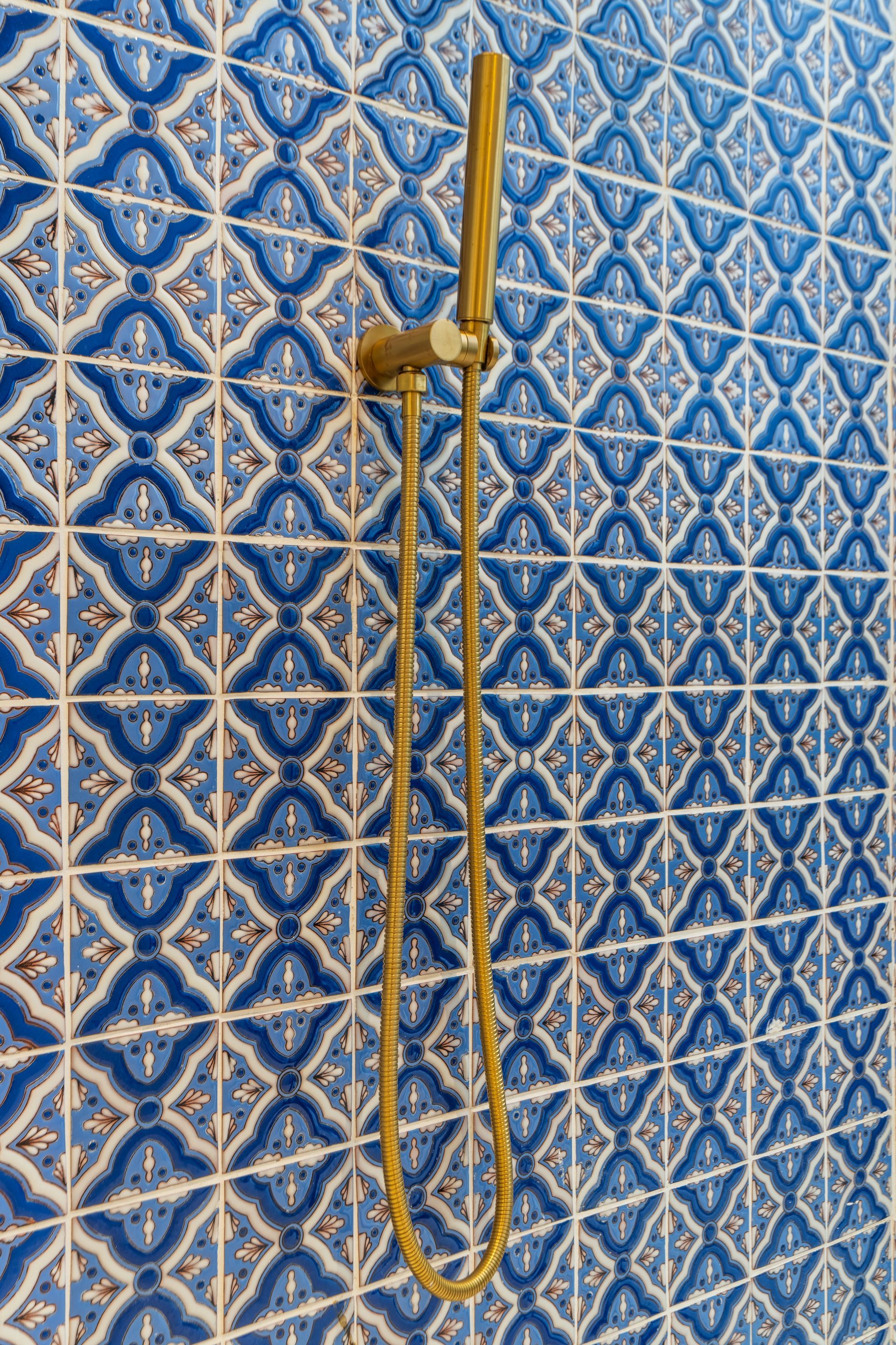 Accesorio de ducha dorado sobre azulejos con estampado azul y blanco.