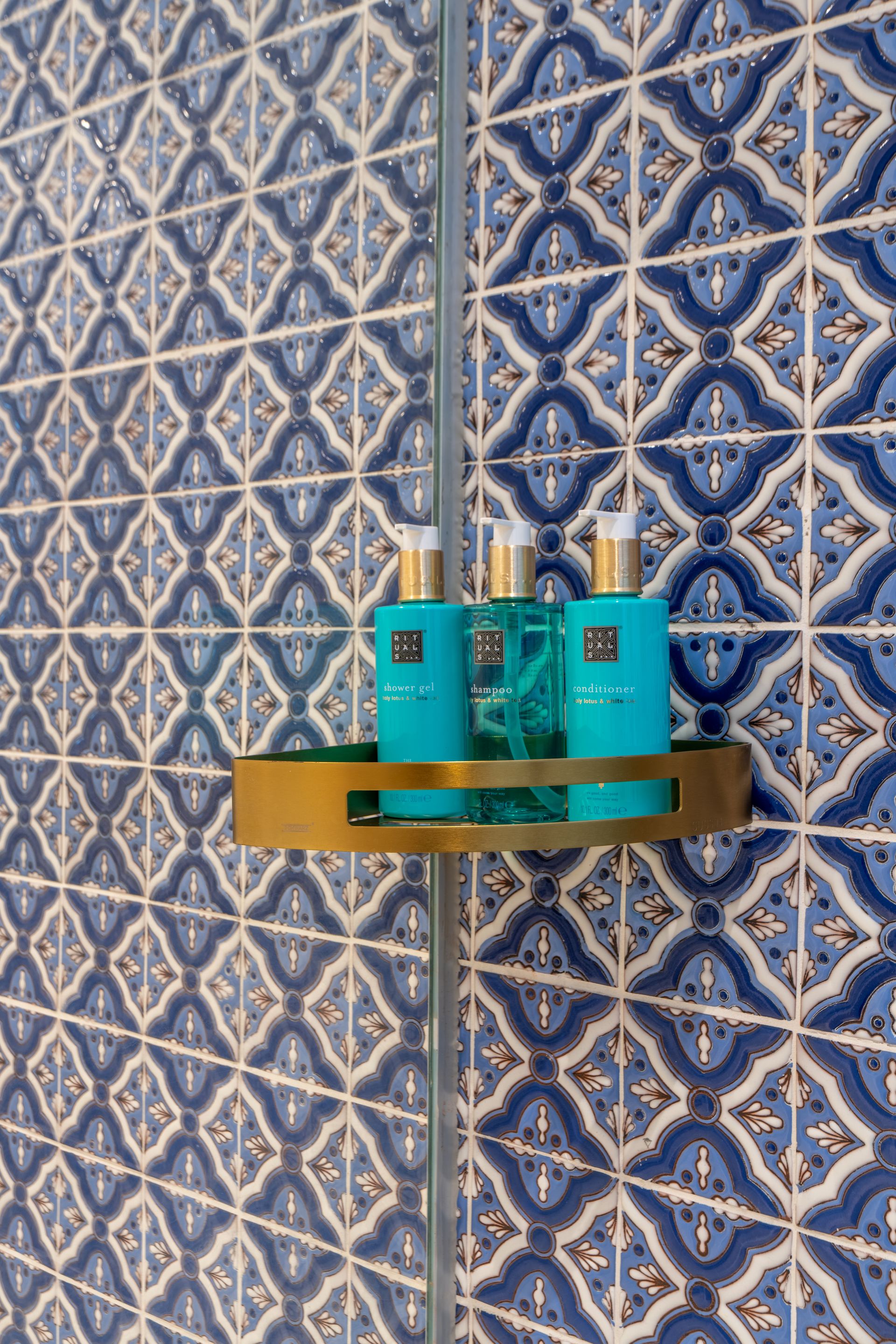 Estante de ducha con botellas de color verde azulado sobre azulejos con dibujos azules.