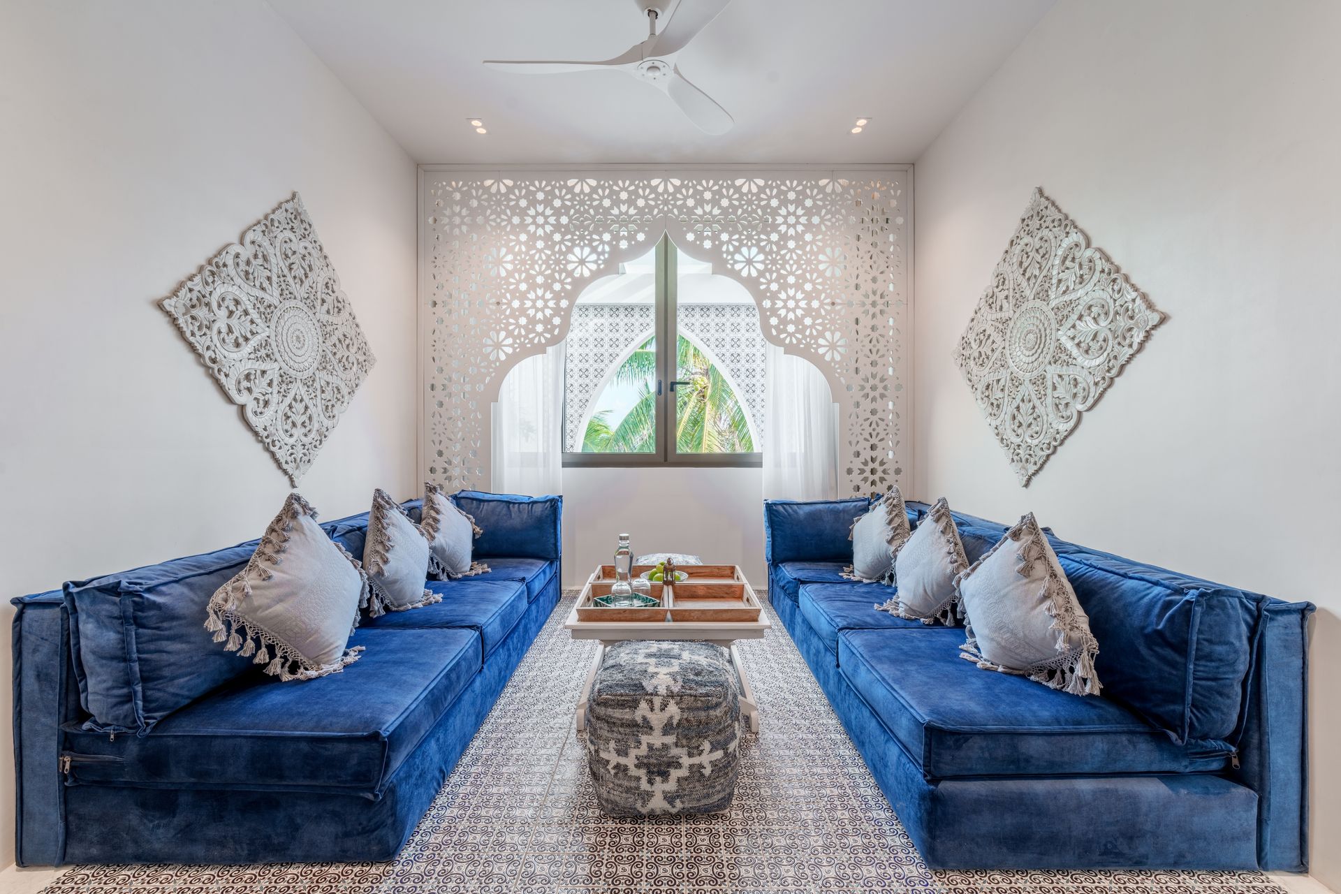 Sala de estar con dos sofás azules, alfombra estampada, paneles de pared decorativos y paredes blancas.