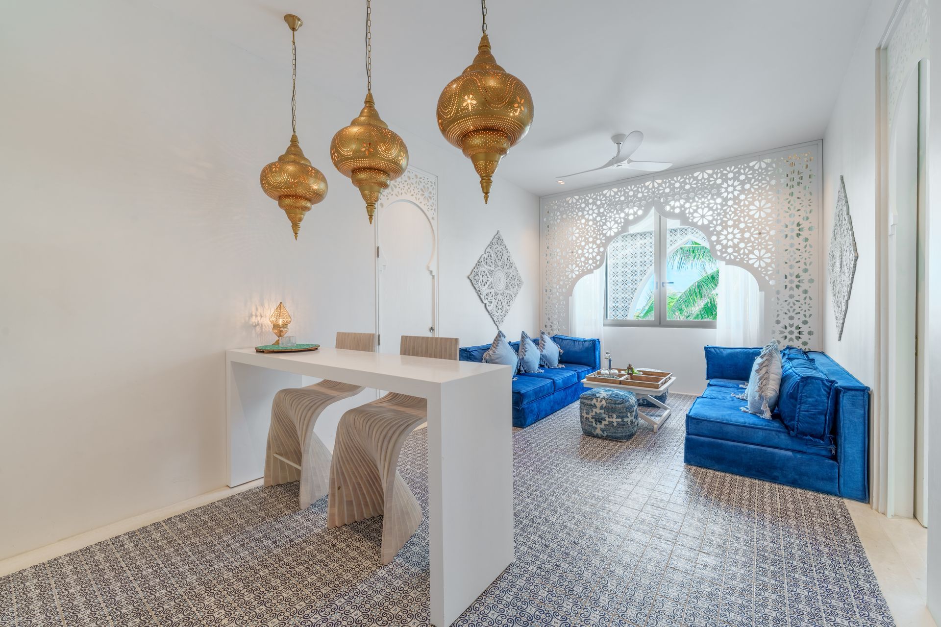 Sala de estar con faroles dorados, sofás azules, paredes blancas y recortes ornamentados.