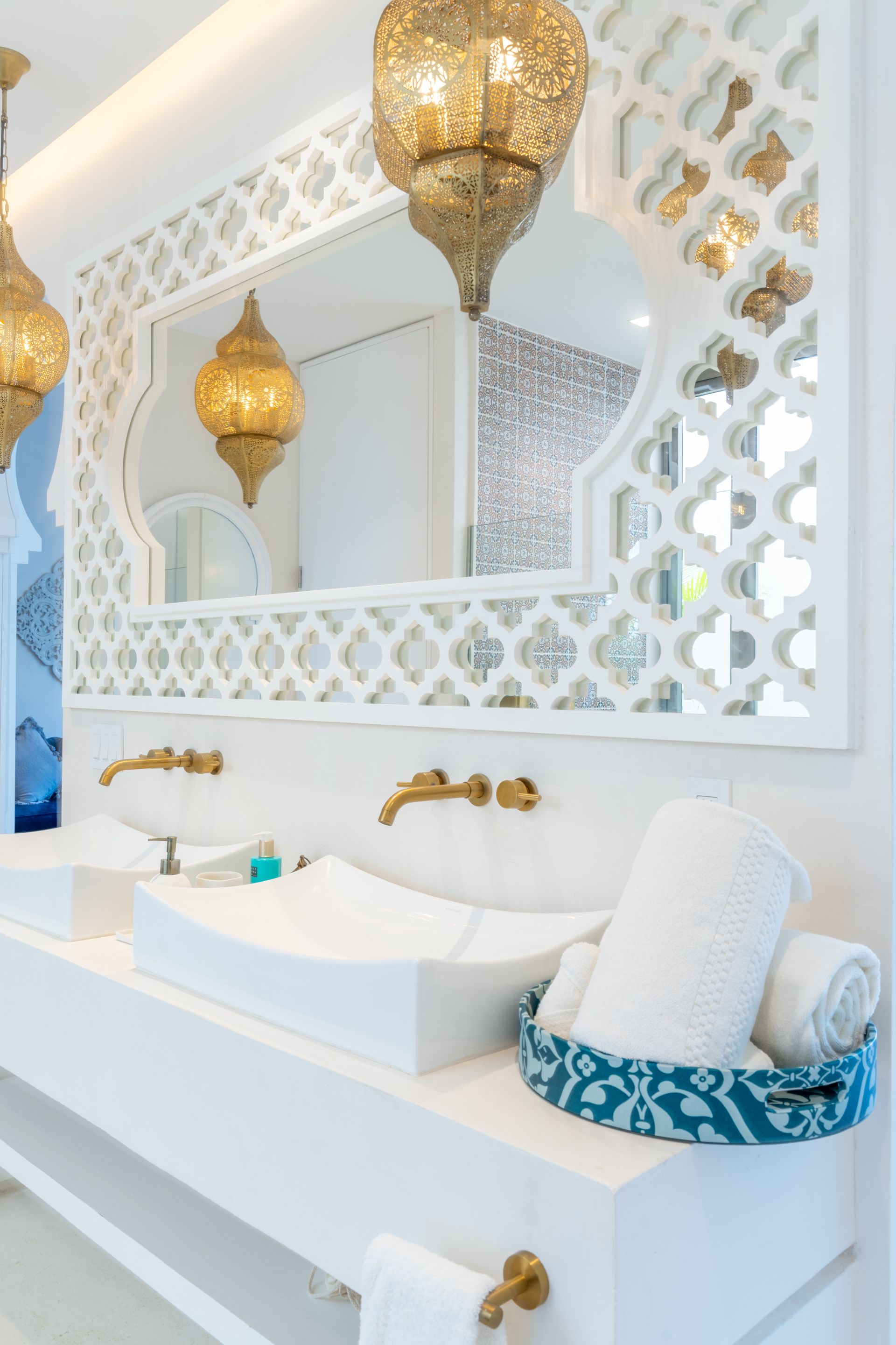 Baño con accesorios de iluminación dorados ornamentados, lavabo blanco, marco de espejo decorativo y toallas en una canasta turquesa.
