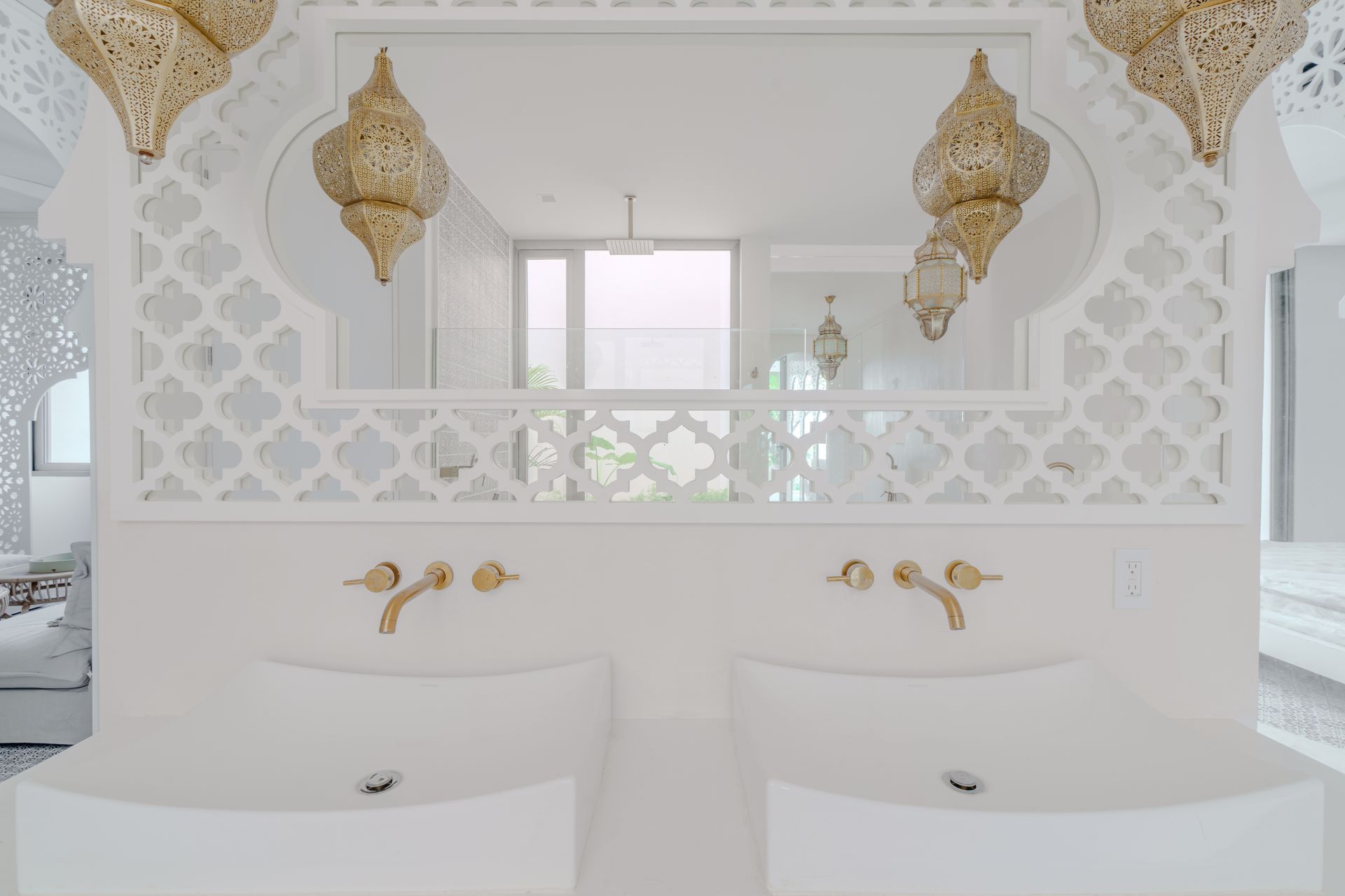 Baño blanco con accesorios de iluminación, lavabos y grifos adornados en color dorado.