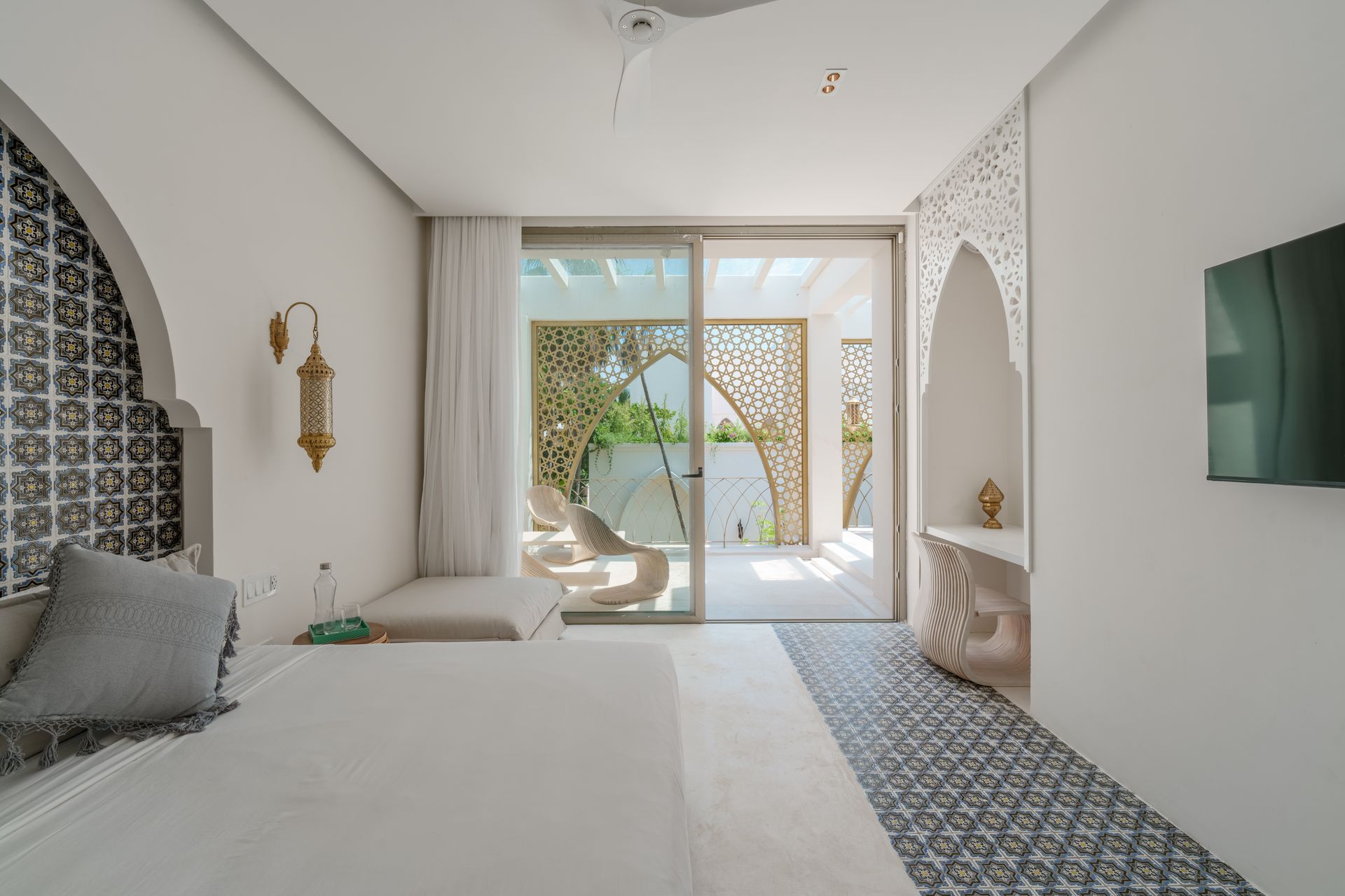 Dormitorio con paredes blancas, arcos ornamentados, puerta corrediza a un patio y piso de baldosas con dibujos decorativos.