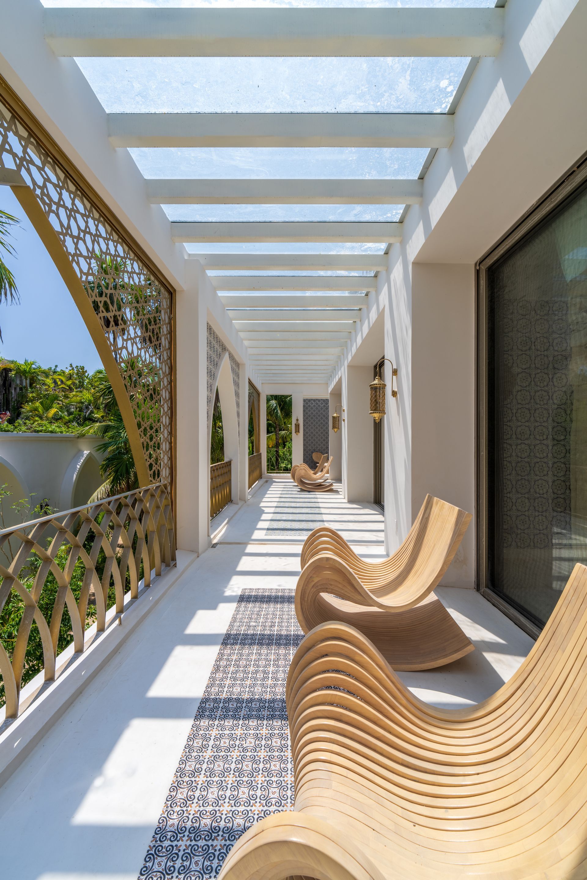 Balcón exterior con sillones de madera clara, barandilla de filigrana dorada y enrejado superior.