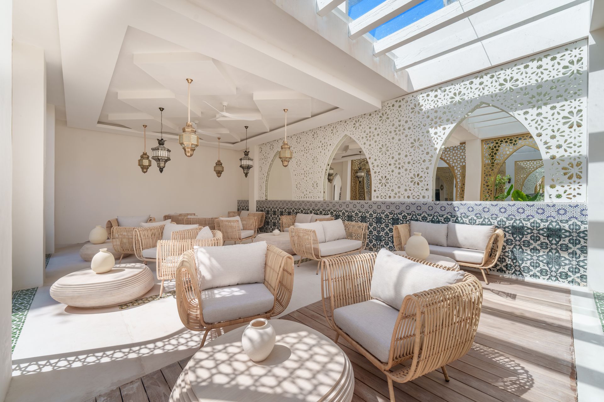 Salón en la azotea con muebles tejidos, decoración blanca y recortes decorativos en las paredes, con luz natural procedente de un tragaluz.
