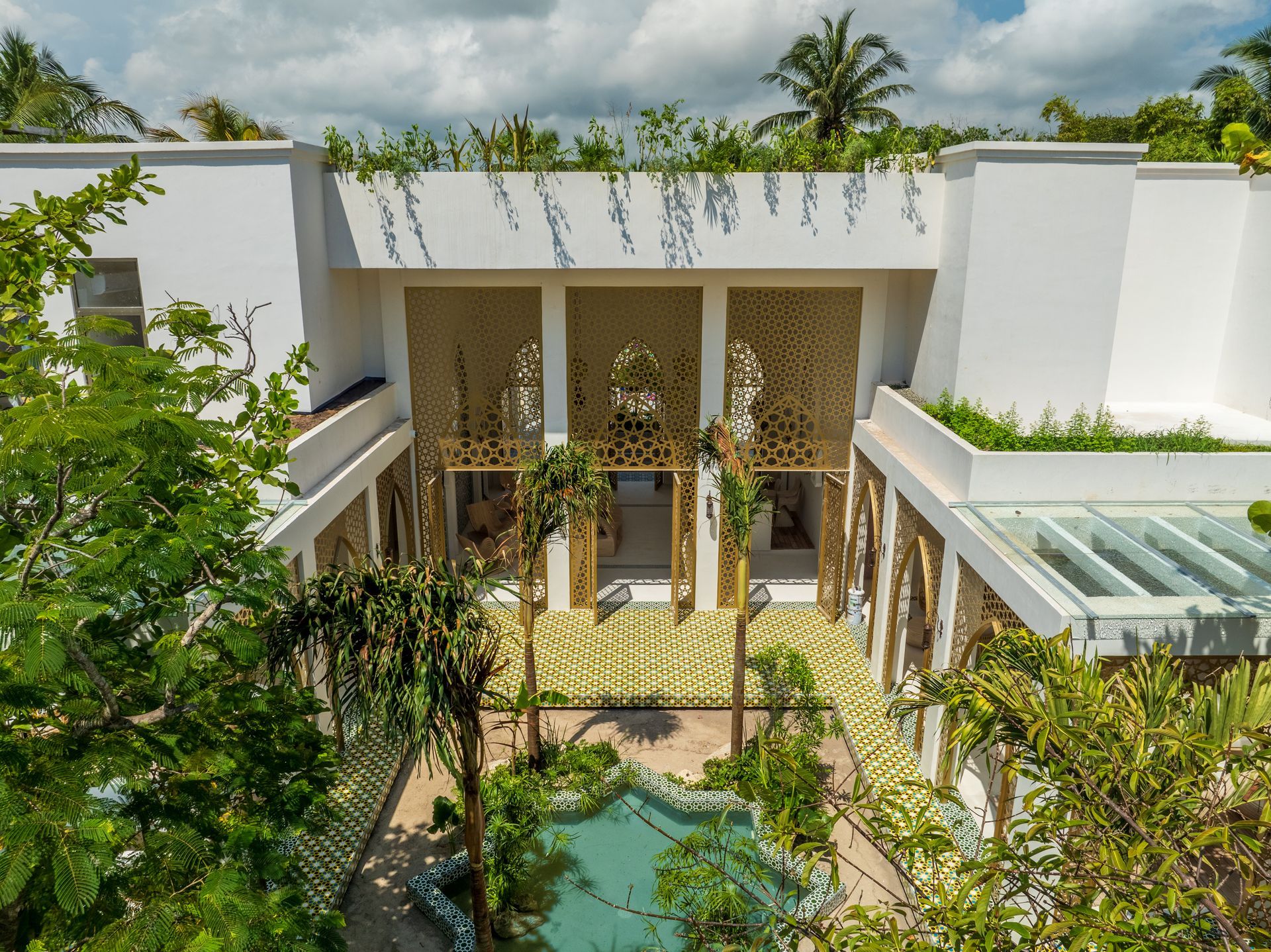 Edificio blanco con detalles ornamentales dorados y una piscina rodeada de vegetación.