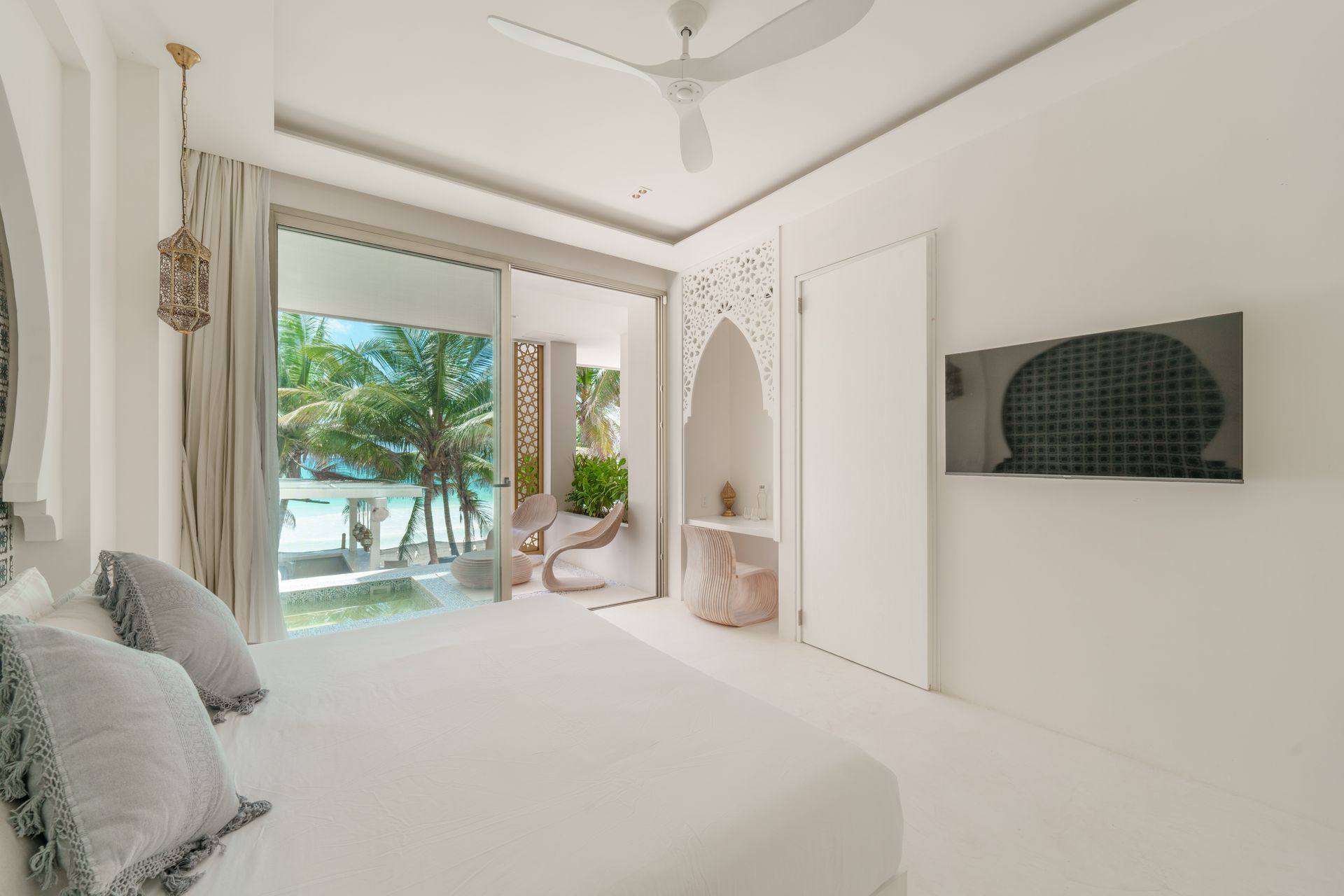 Dormitorio blanco luminoso con cama, TV y balcón con vista a la playa.