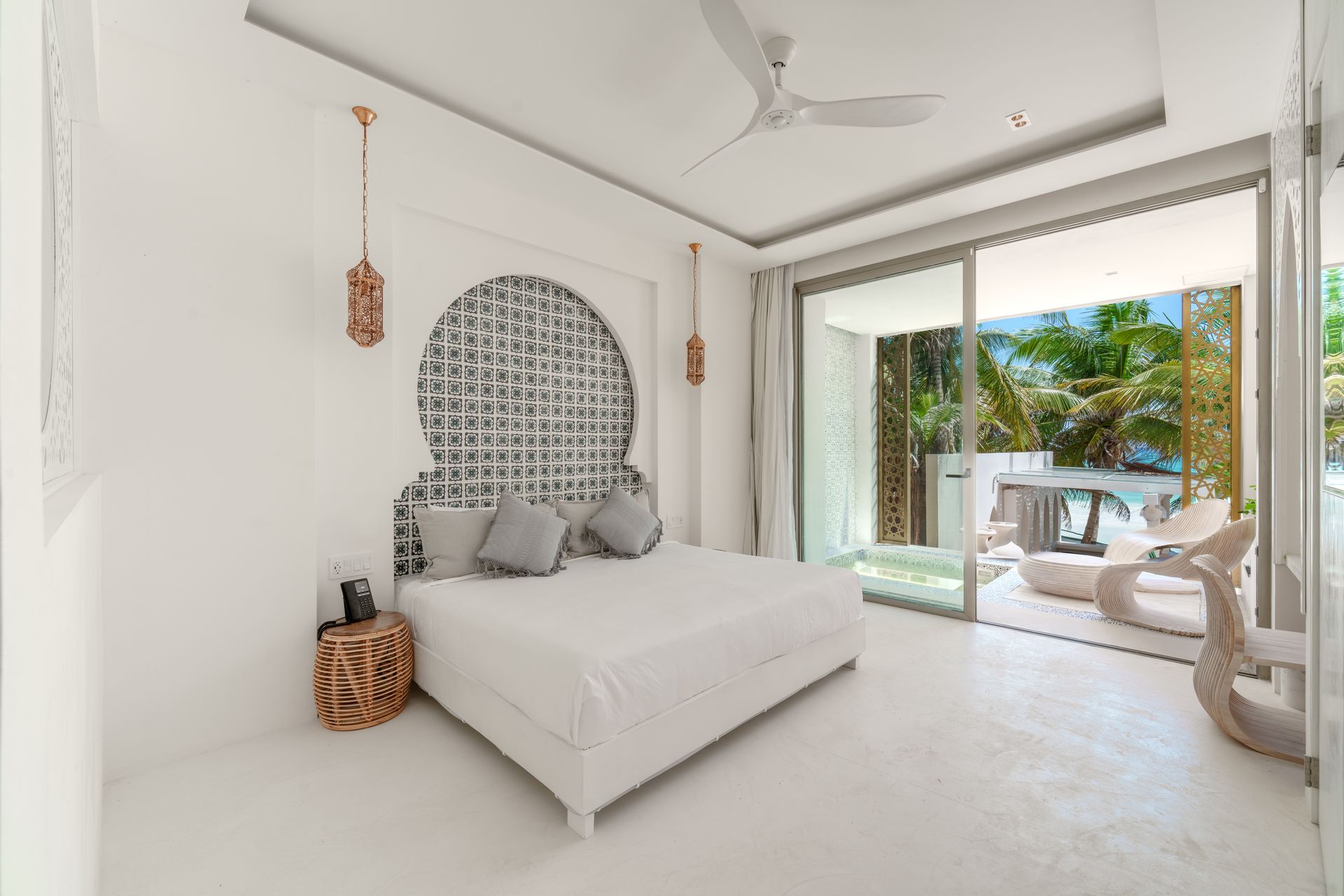 Dormitorio blanco con una cama grande, cabecera decorativa y puerta corrediza de vidrio que conduce a una zona de estar al aire libre.
