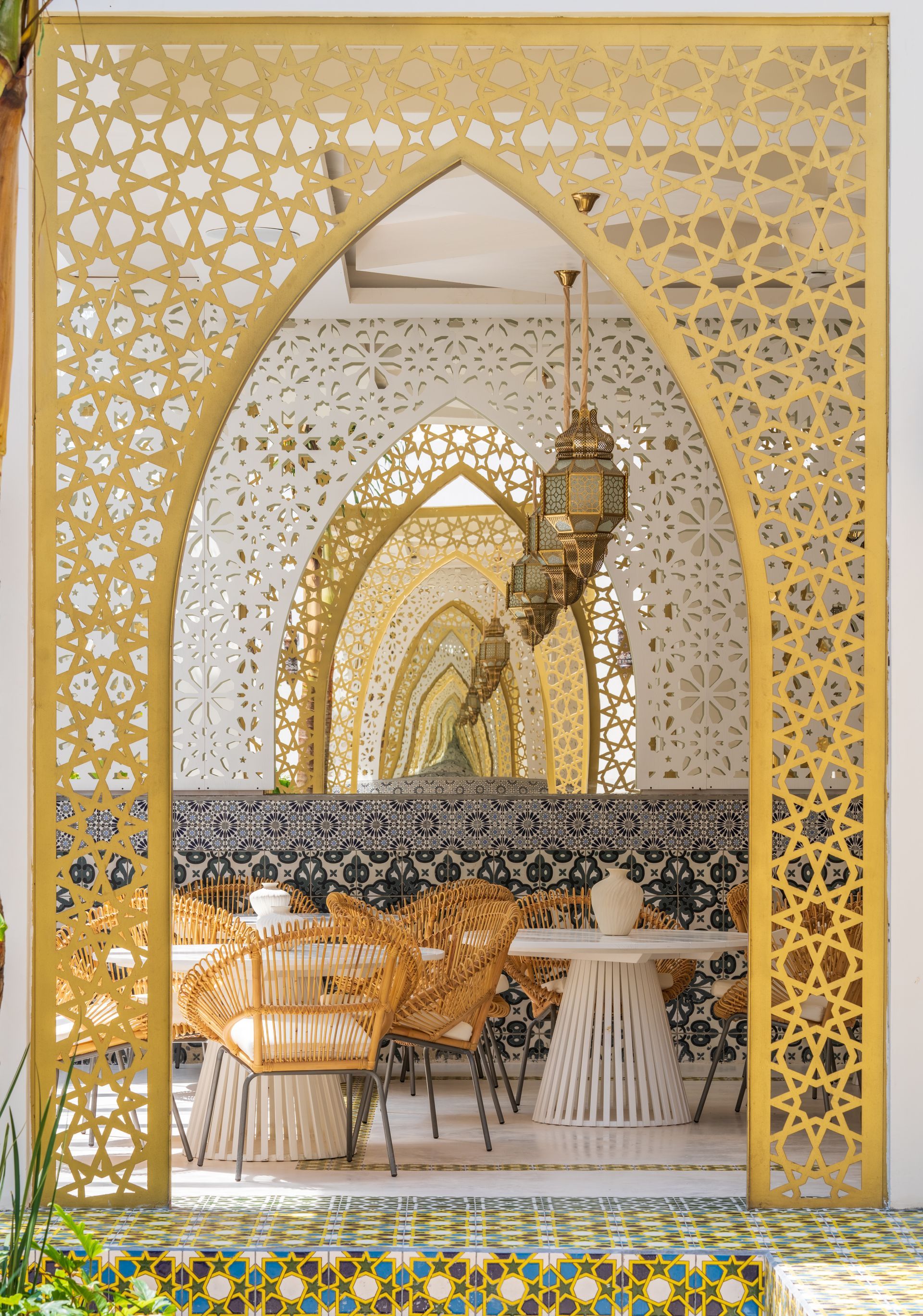 Arcos arabescos que enmarcan el interior de un restaurante con sillas de ratán y linternas ornamentadas.