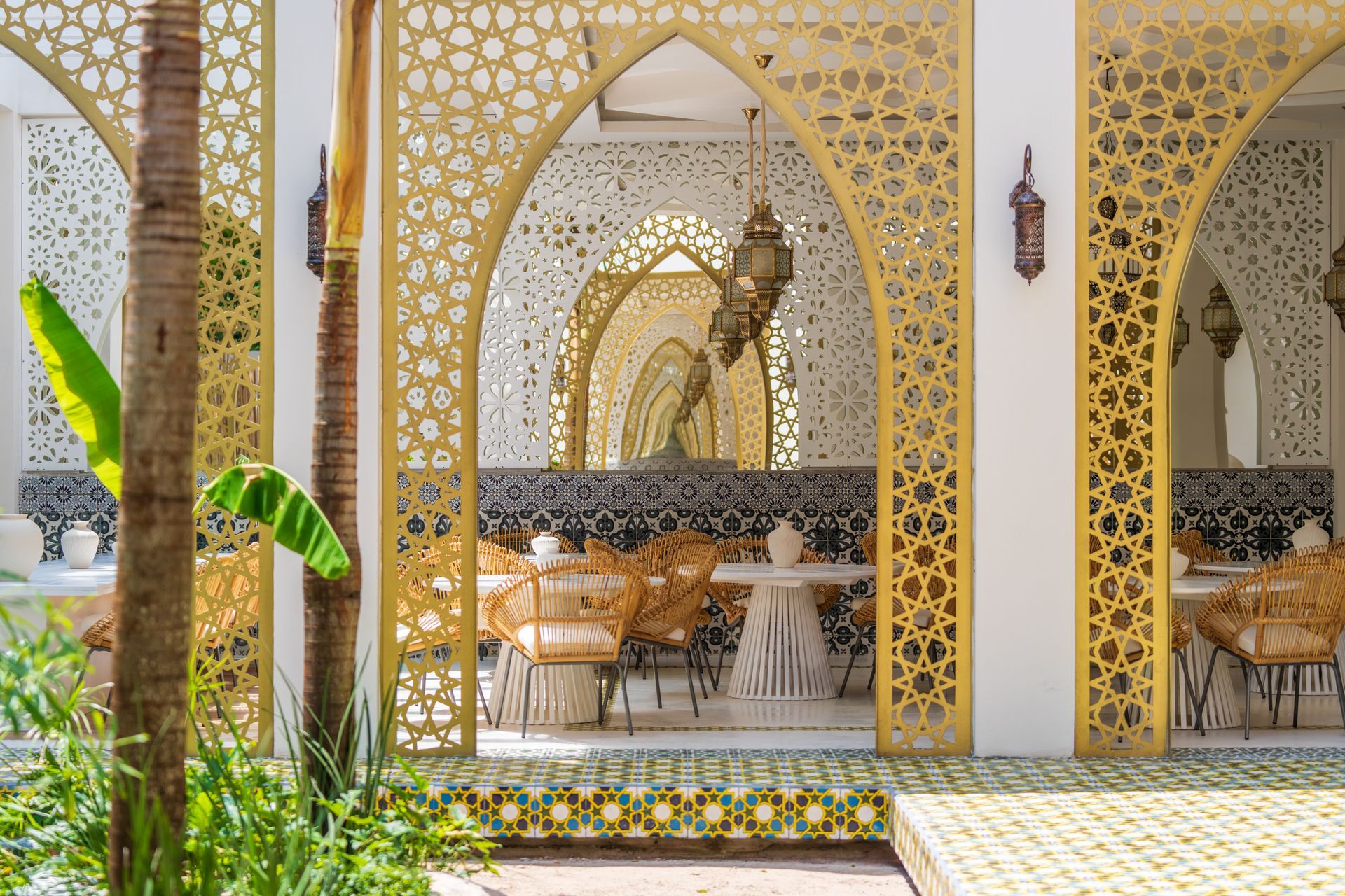 Restaurante al aire libre con arcos de filigrana dorada, sillas de mimbre y azulejos intrincados.