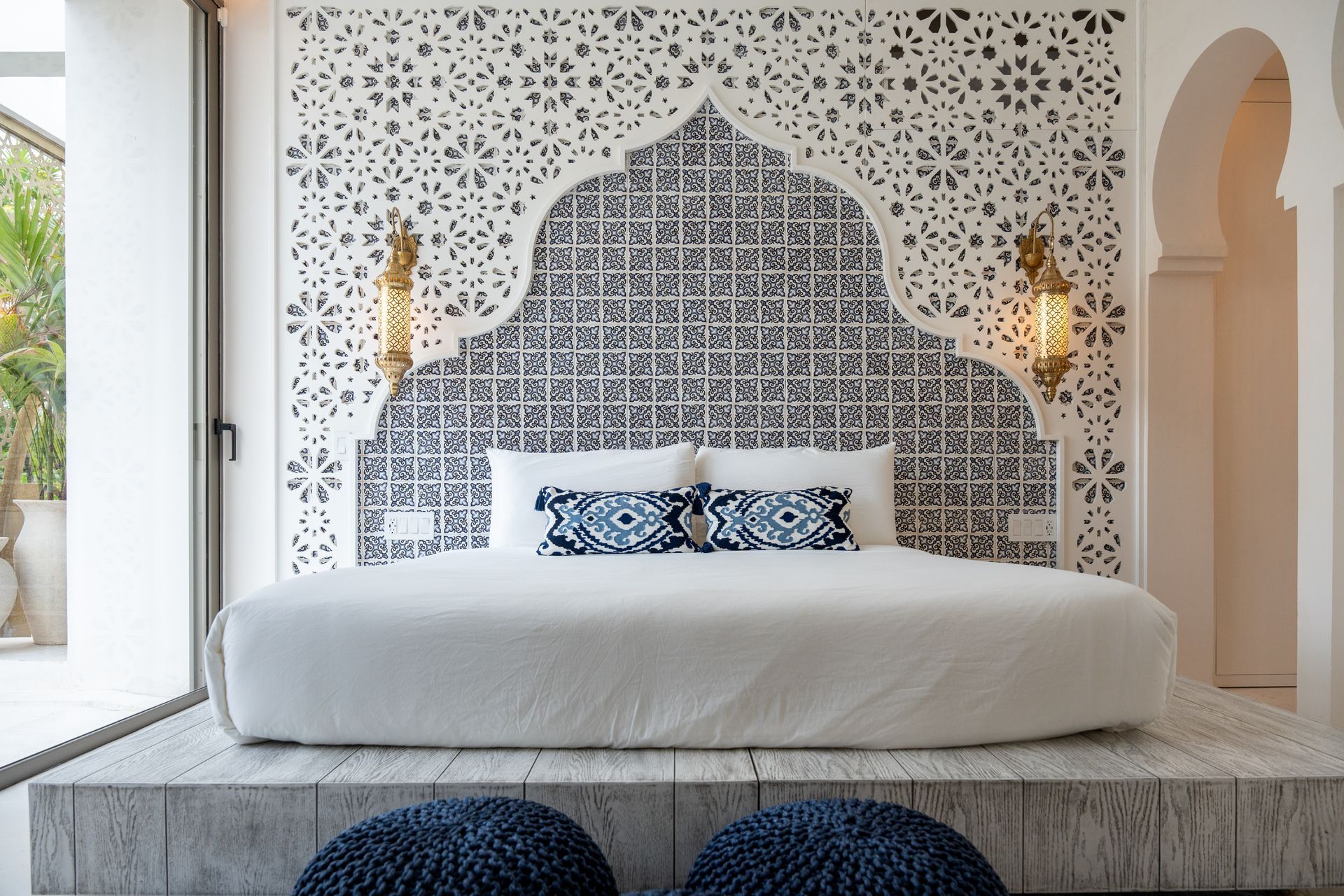 Bedroom with a white bed, ornate blue and white patterned headboard, and blue poufs.