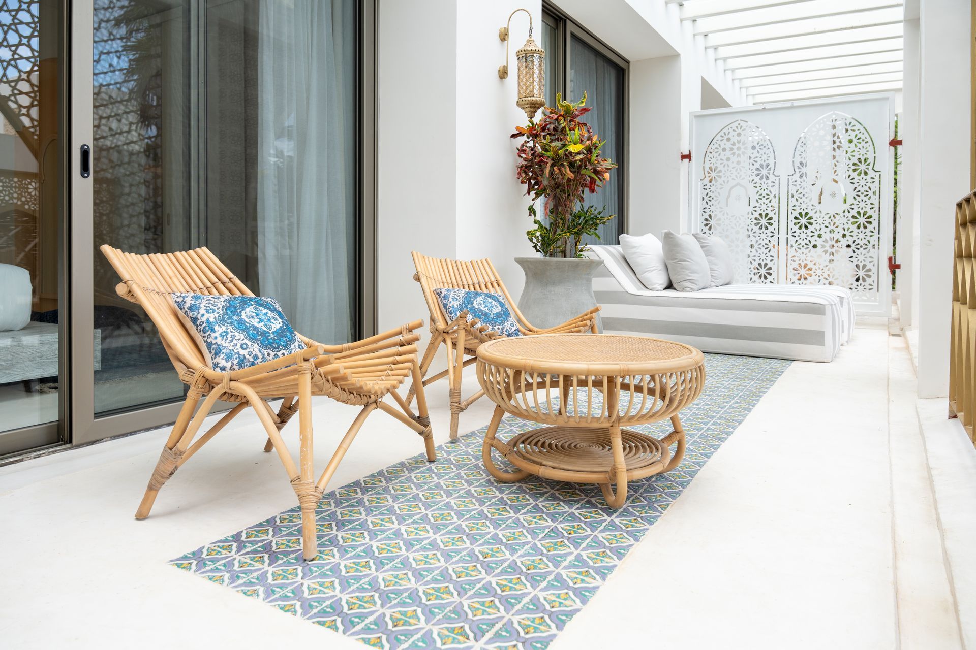 Patio con sillas de bambú, mesa de café, alfombra estampada azul y diván blanco.
