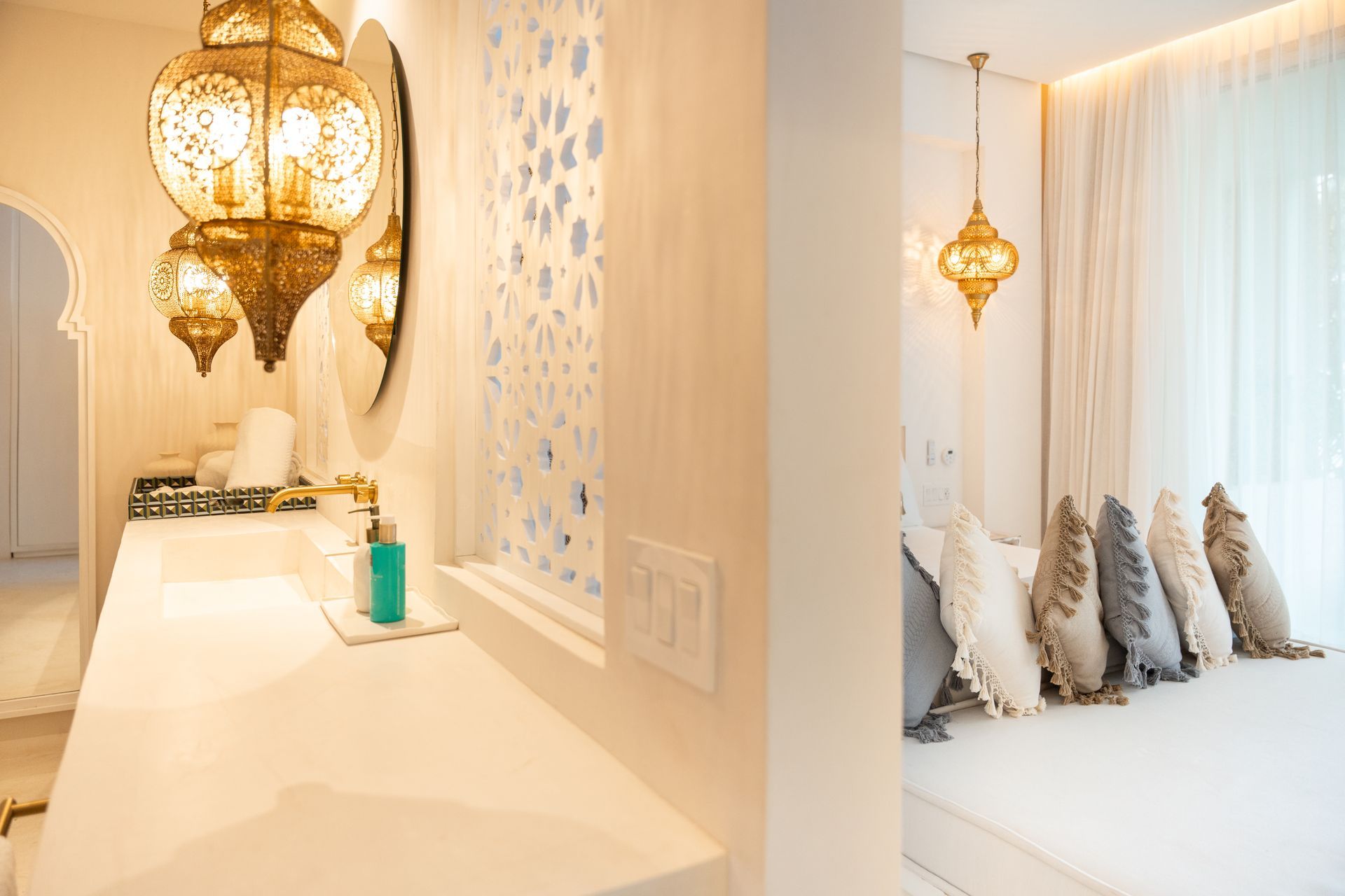 Elegante baño con faroles dorados ornamentados, pared decorativa y una vista de un dormitorio con almohadas.