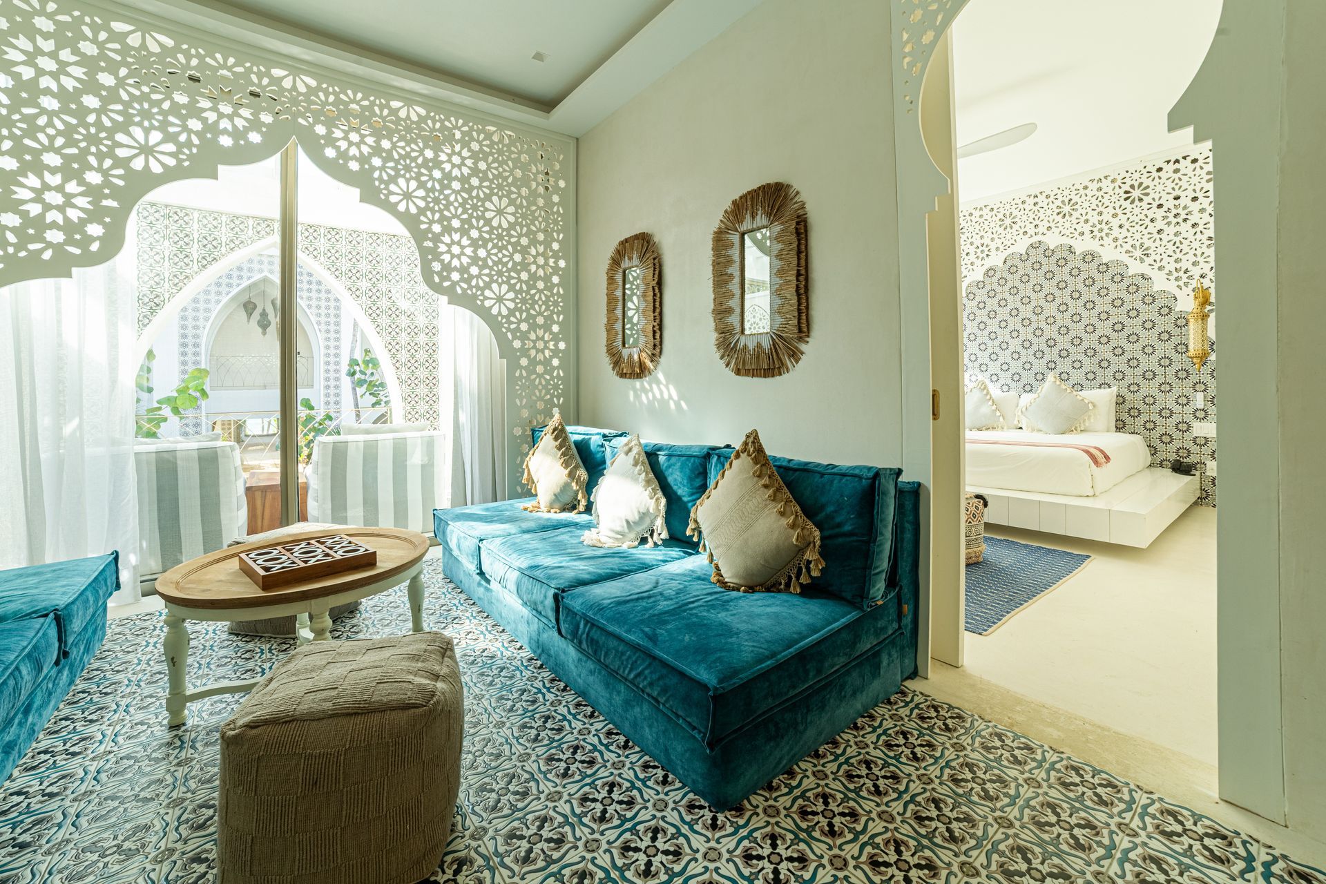 Sala de estar con sofá verde azulado, alfombra estampada, ventana con arco decorativo y dormitorio contiguo.