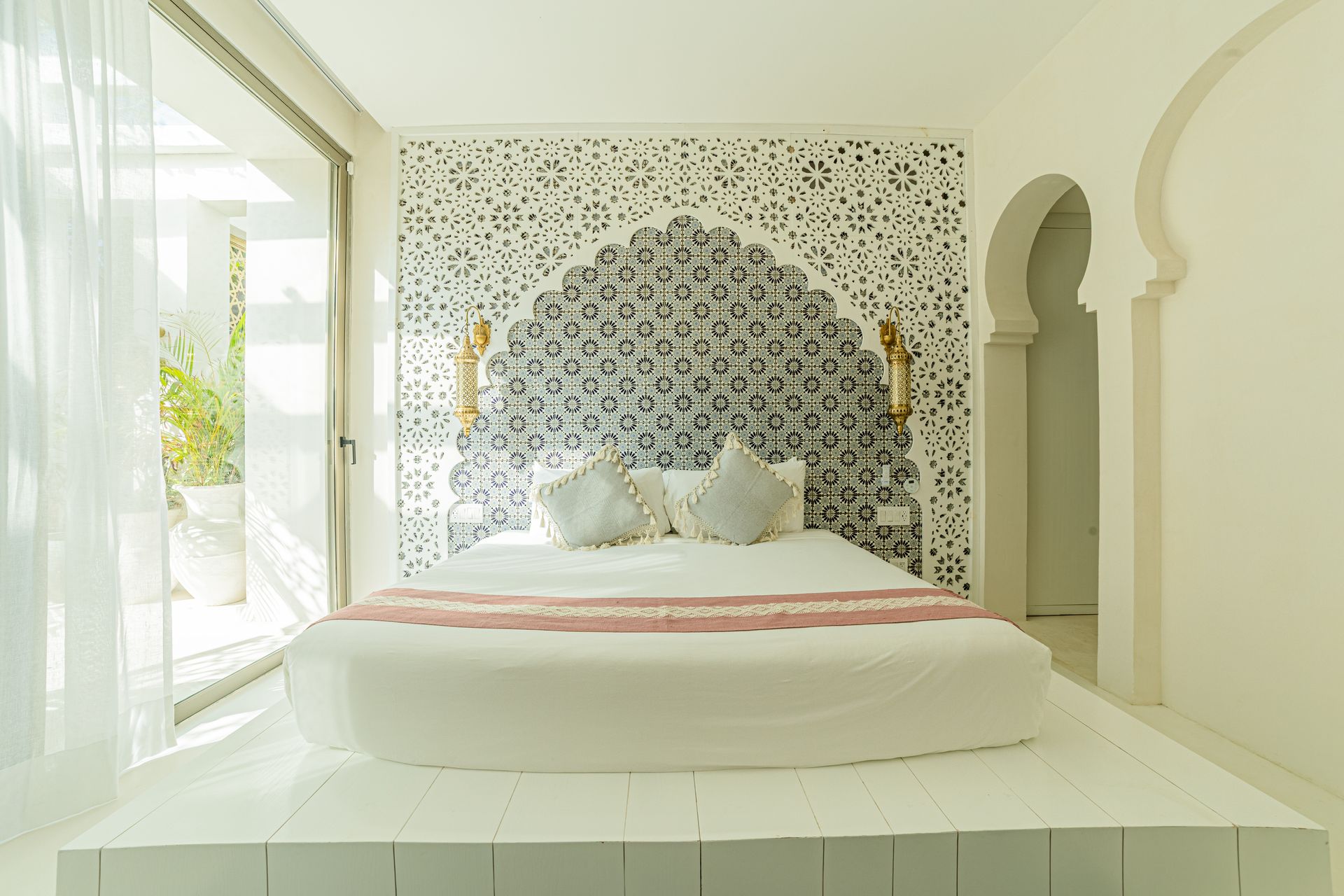 Dormitorio con detalles arqueados, cabecero decorativo y puerta corrediza a un balcón. Tonos blancos y grises.