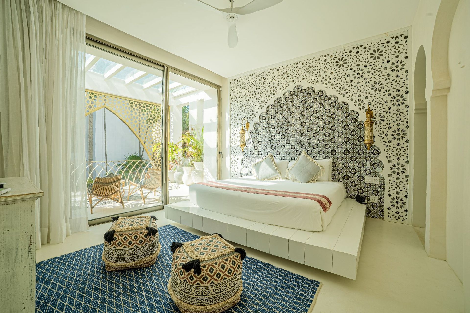 Dormitorio con cama de plataforma blanca, cabecera estampada, alfombra azul y acceso a patio exterior.