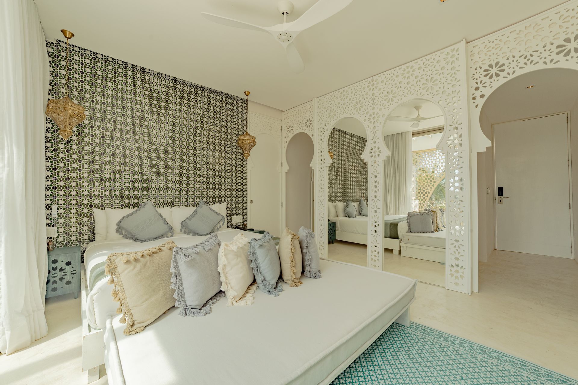 Dormitorio con arco tallado en blanco, pared estampada, cama con almohadas y diván.