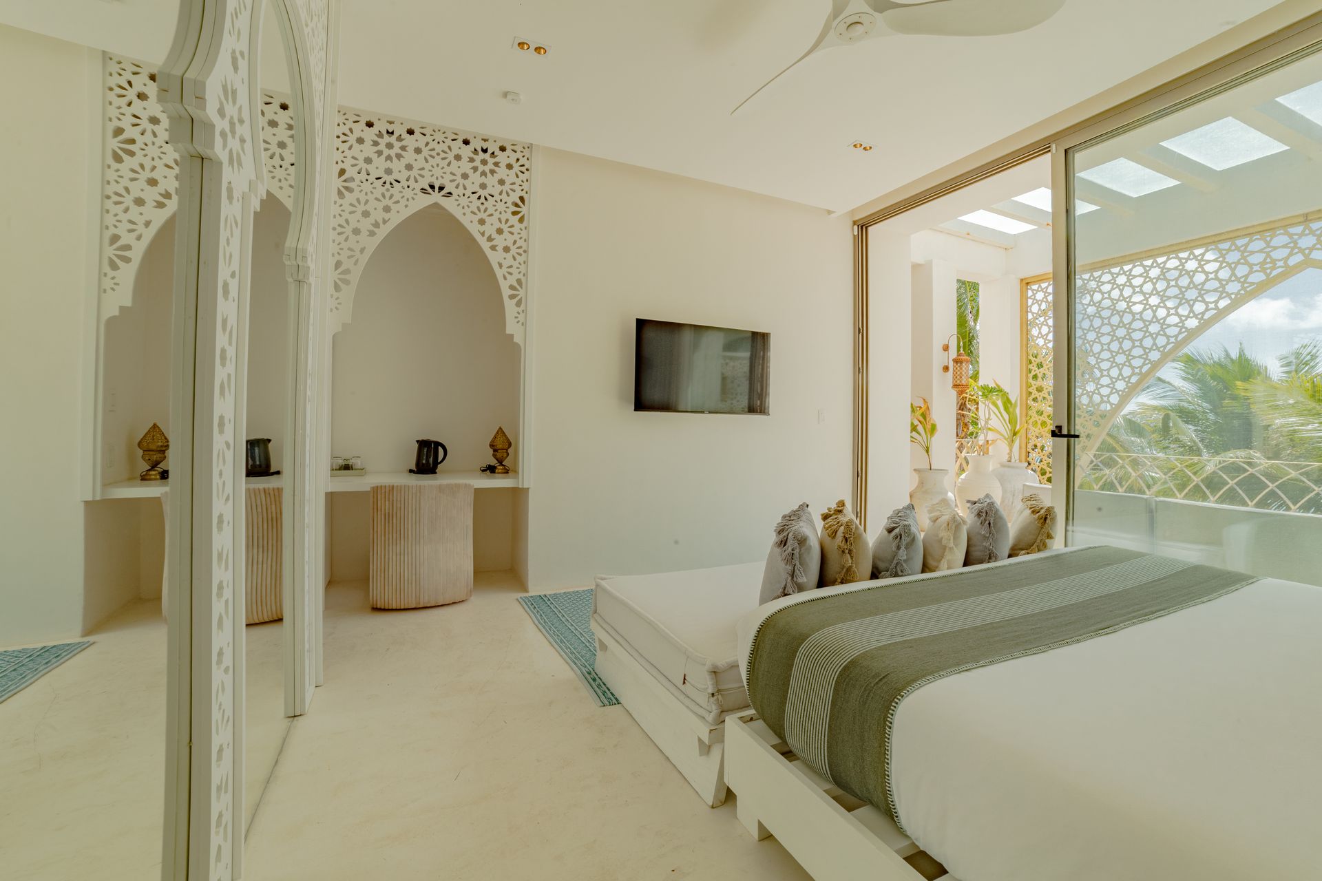 Dormitorio blanco luminoso con arcos tallados, una cama y puertas corredizas a un balcón.