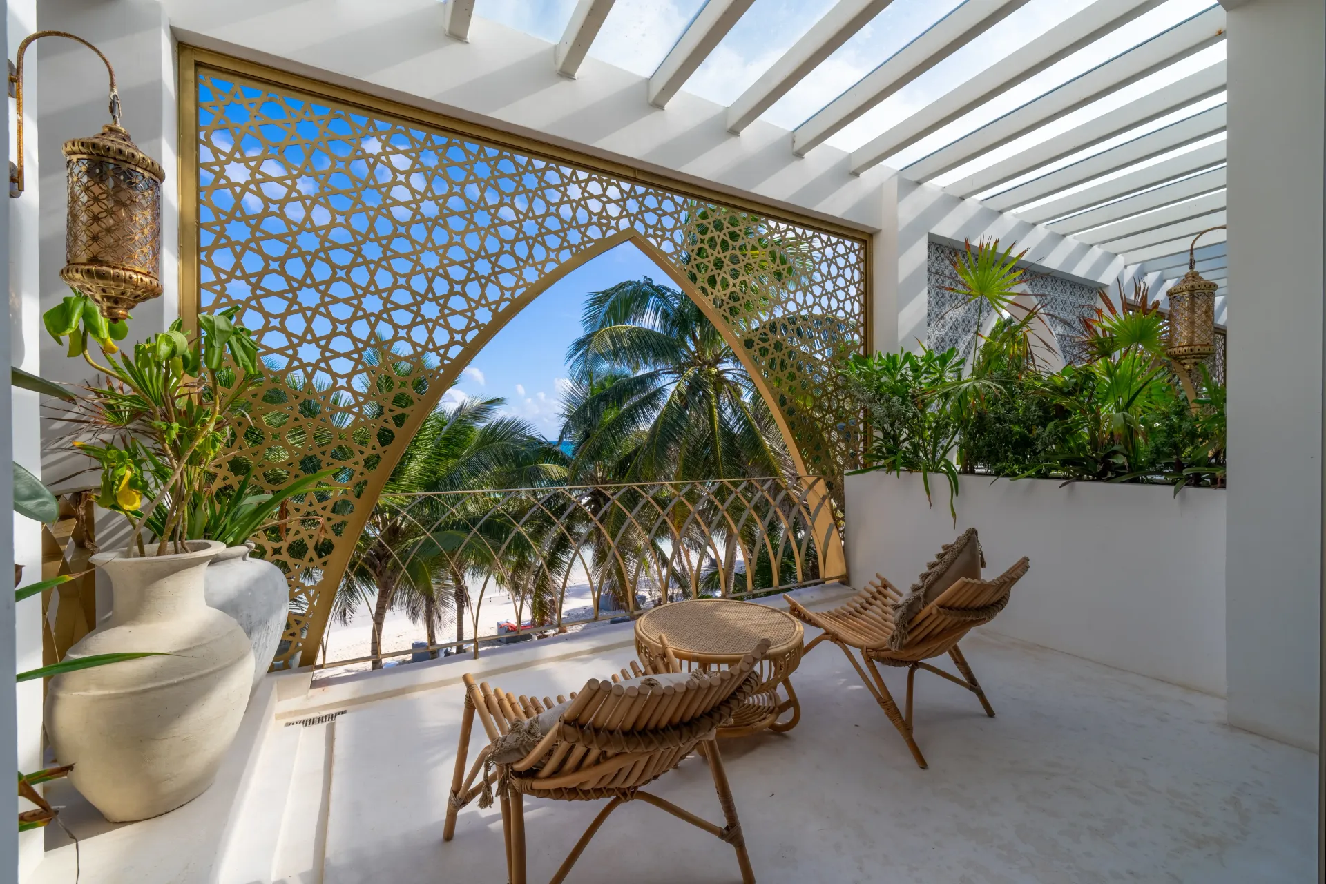 Balcón con muebles de ratán, mampara dorada, plantas y vista a palmeras y al mar.