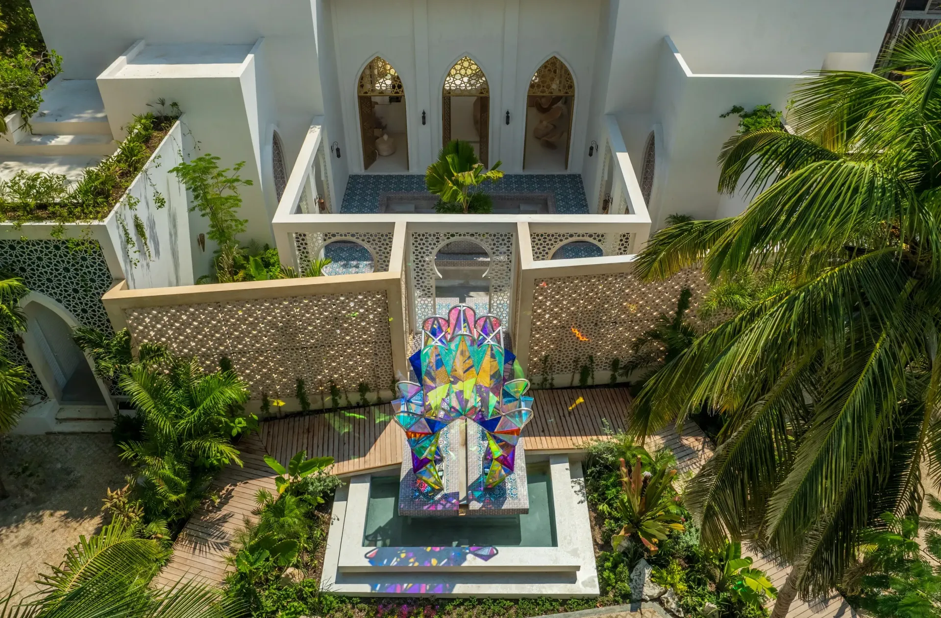 Edificio blanco con arcos y diseños intrincados, una escultura colorida al frente, rodeada de vegetación.