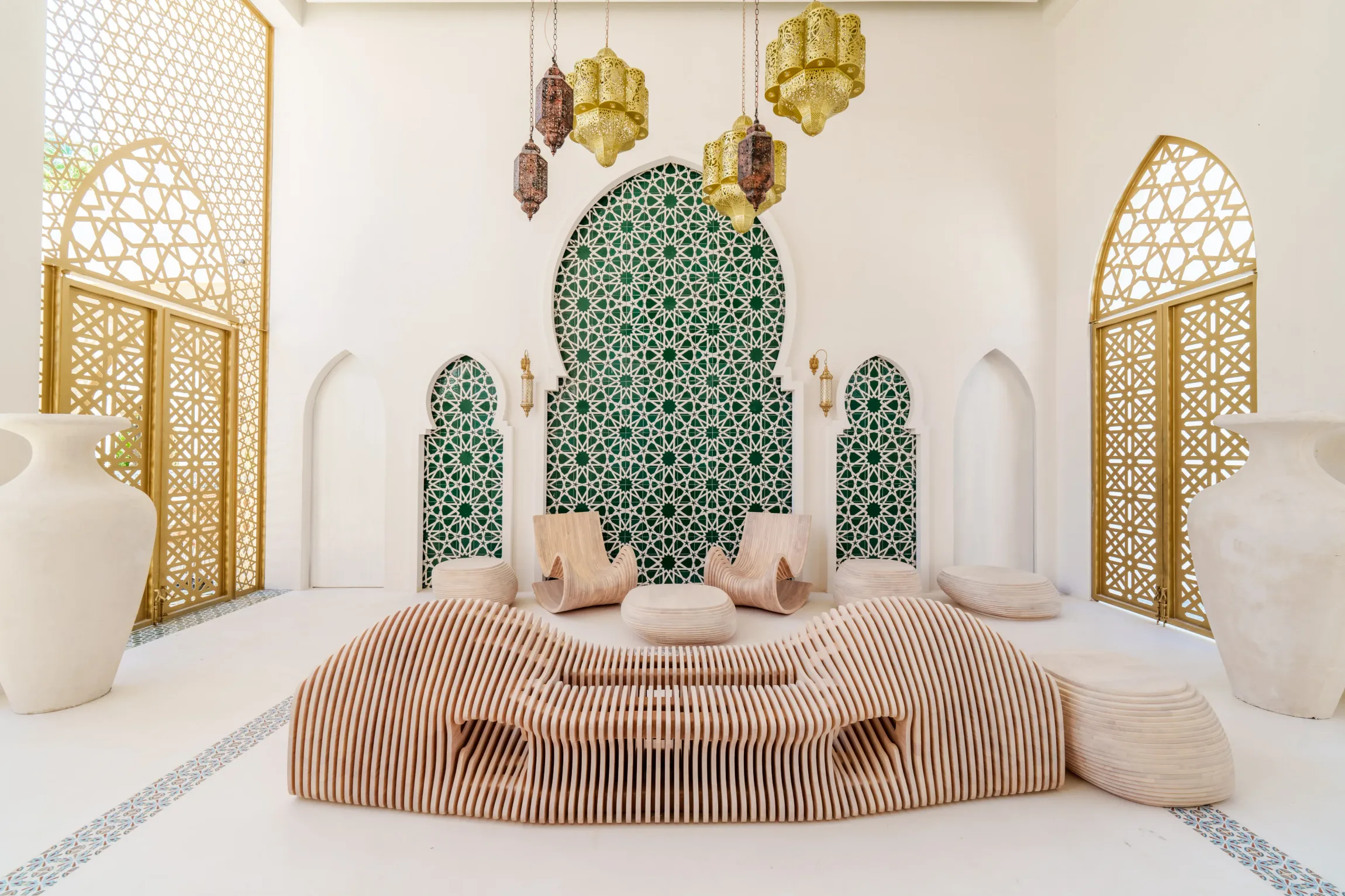 Elegant Moroccan-style lounge with carved wood seating, gold accents, green mosaic wall  and decorative hanging lamps.