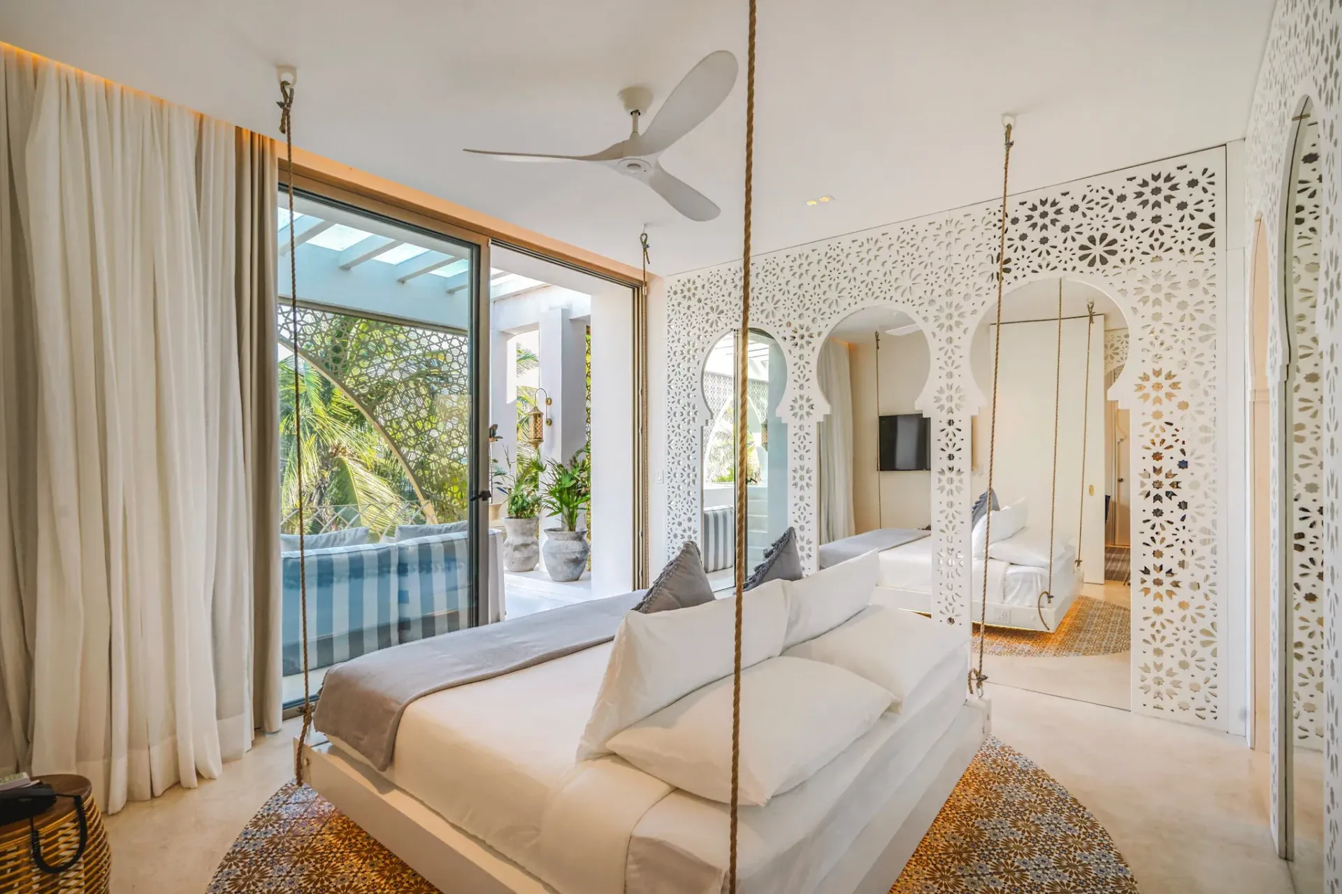 Dormitorio blanco con cama abatible, pared recortada ornamentada y puertas corredizas que dan a un patio.