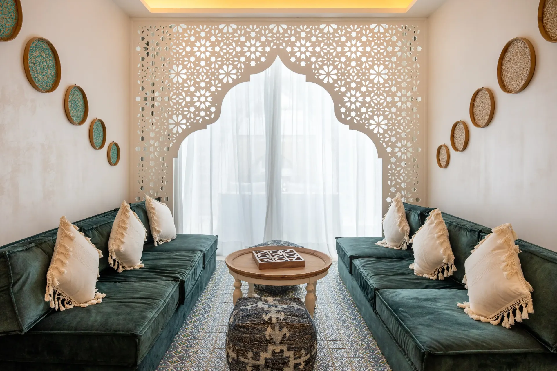 Sala de estar con sofás verde azulado, arco blanco intrincado, adornos de pared decorativos y mesa de café redonda.