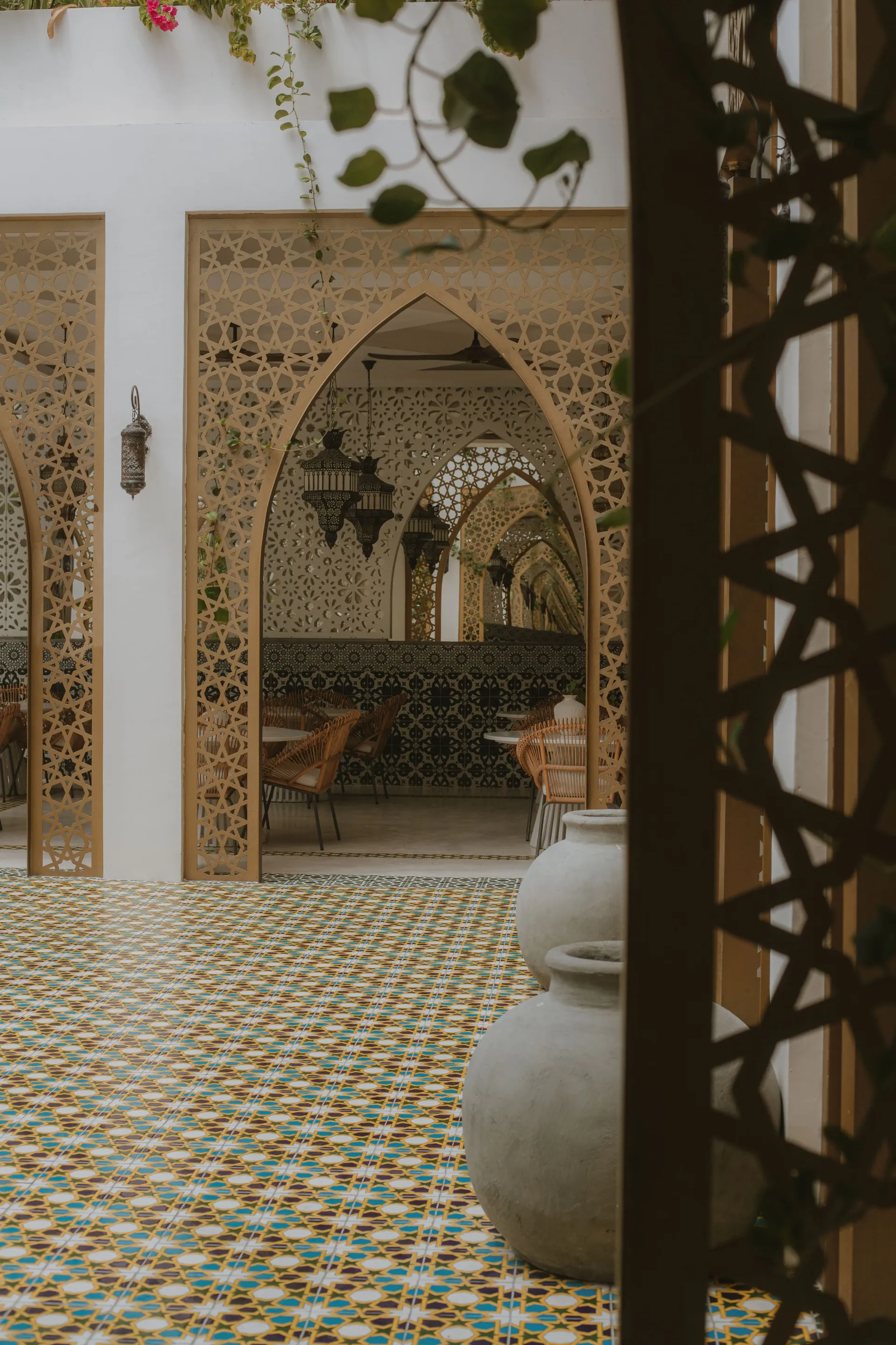 An interior courtyard with intricate lattice archways, patterned mosaic tiles, and two large ceramic pots.
