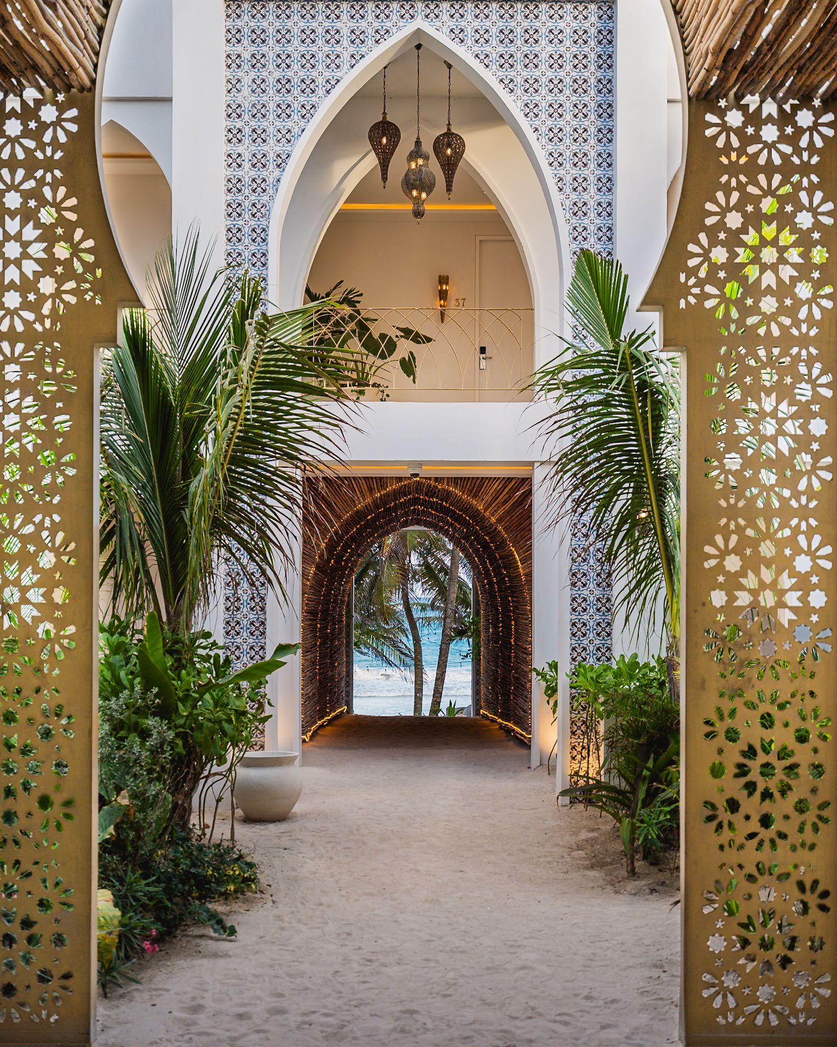 Camino que conduce a una playa enmarcada por arcos ornamentados y exuberante vegetación.