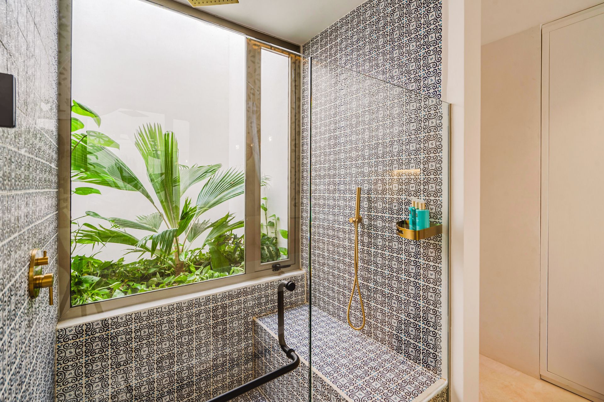 Ducha con paredes de mosaico y ventana con vista a la vegetación.