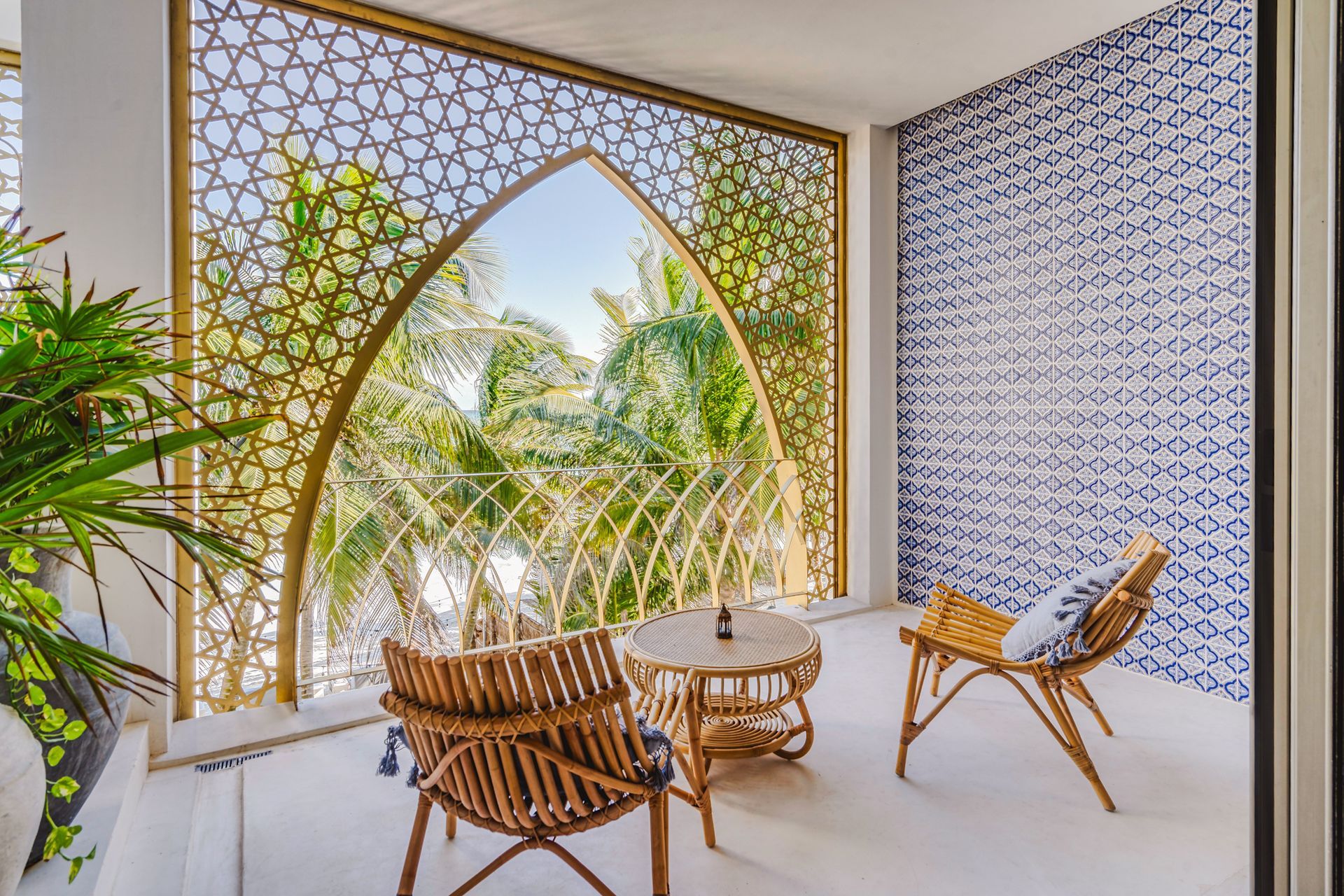 Balcón con muebles de ratán, mampara estampada, pared de azulejos azules y vista a la vegetación.