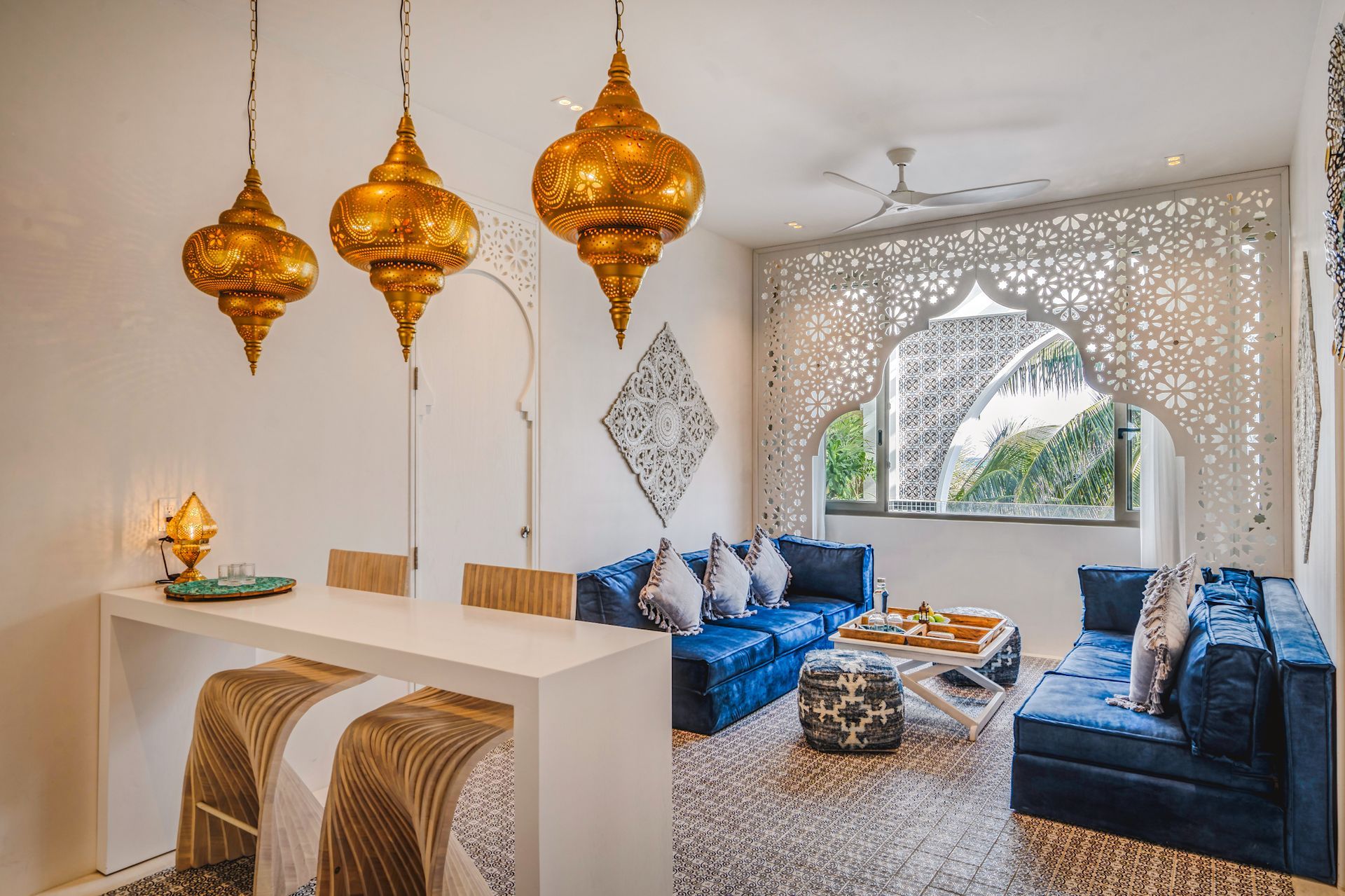 Sala de estar con faroles dorados ornamentados, sofás azules y un arco blanco decorativo.