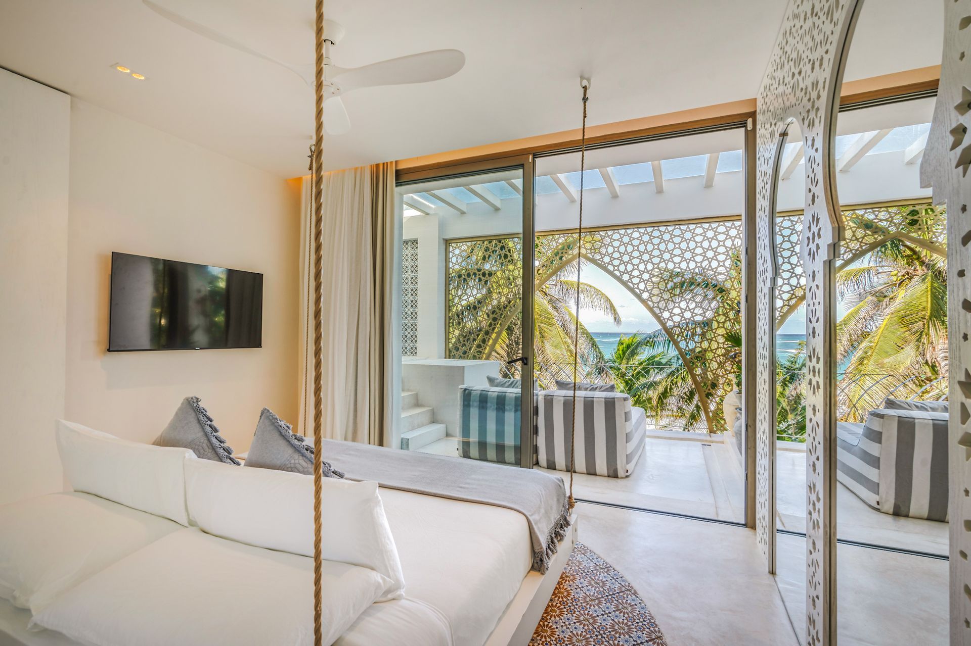 Dormitorio luminoso con vista al mar, cama columpio y panel decorativo de pared.
