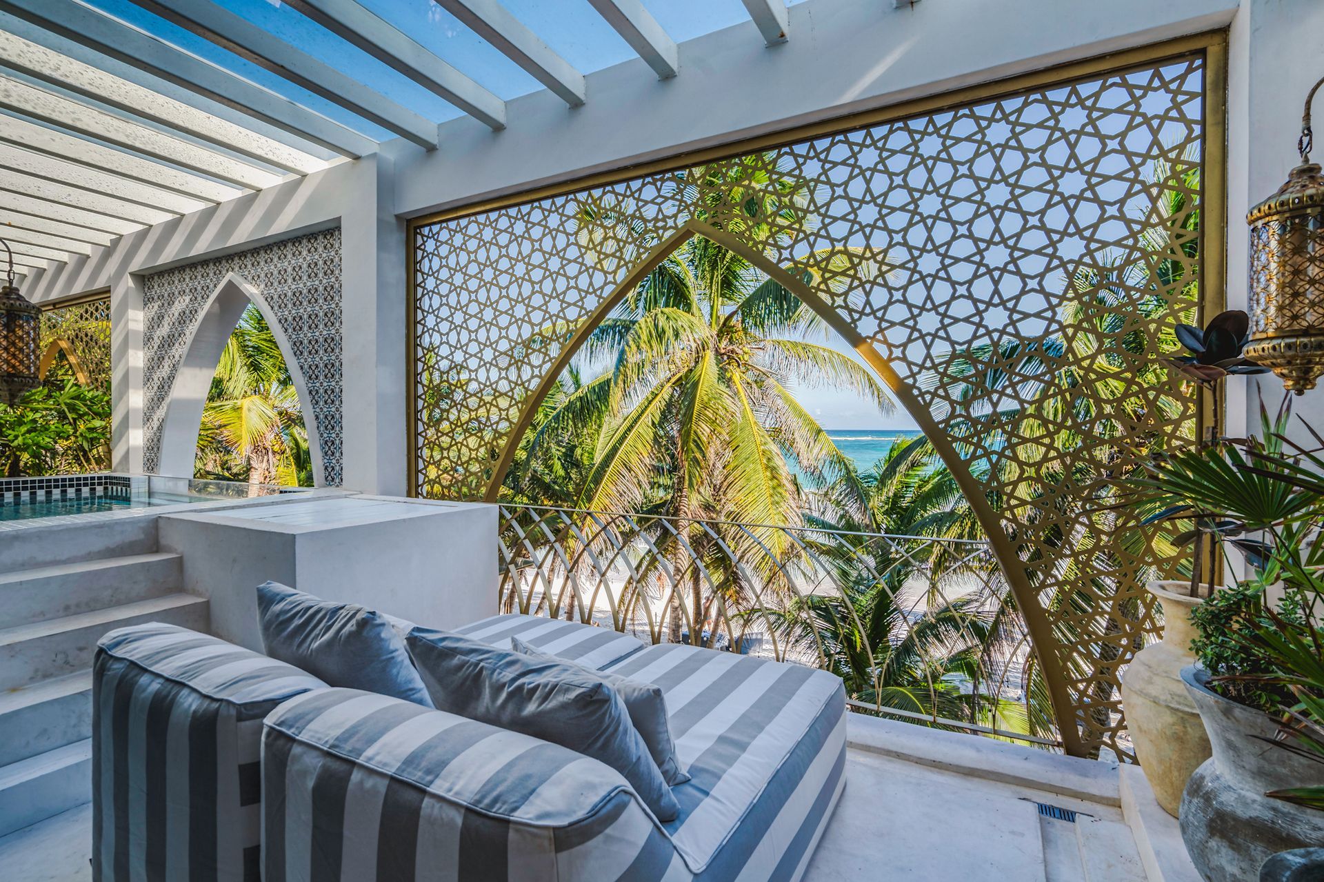 Zona de estar al aire libre con mampara estampada, palmeras y vista al mar.
