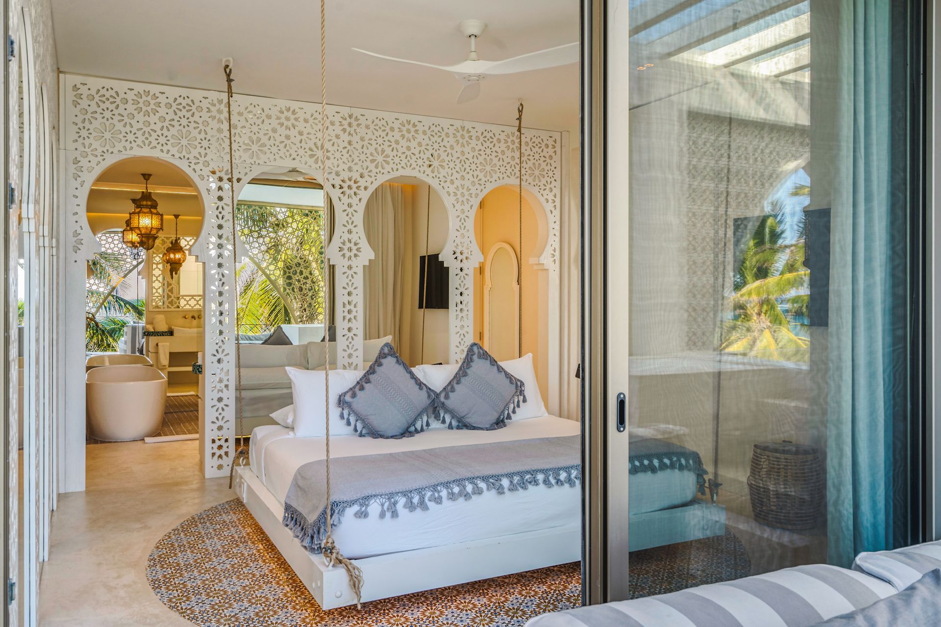 Dormitorio con arco blanco adornado, cama con almohadas grises, puerta corrediza abierta a la vista del exterior.