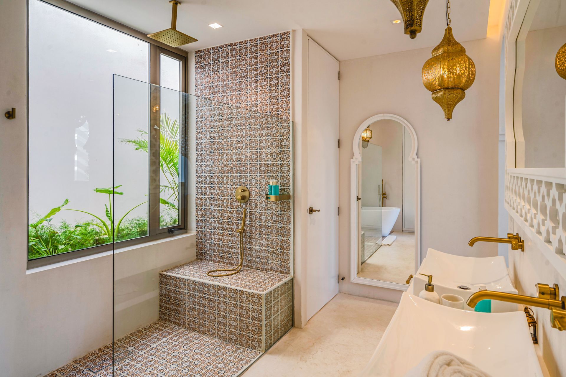 Bathroom with mosaic tile shower, pebble floor, white sink with gold fixtures, and Moroccan lamps.