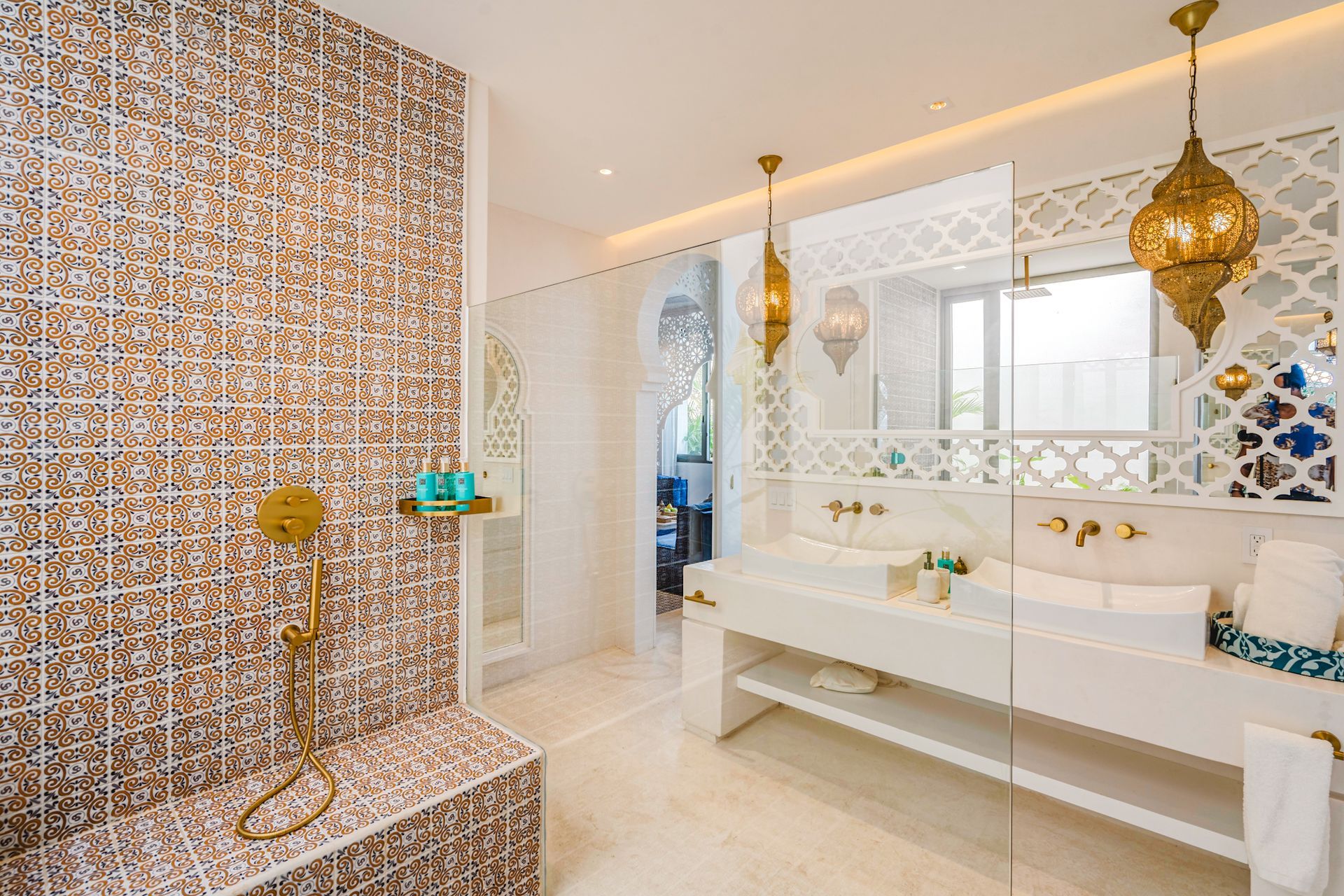 Moroccan-style bathroom with patterned tile, gold fixtures, hanging lanterns, and a glass-enclosed shower.