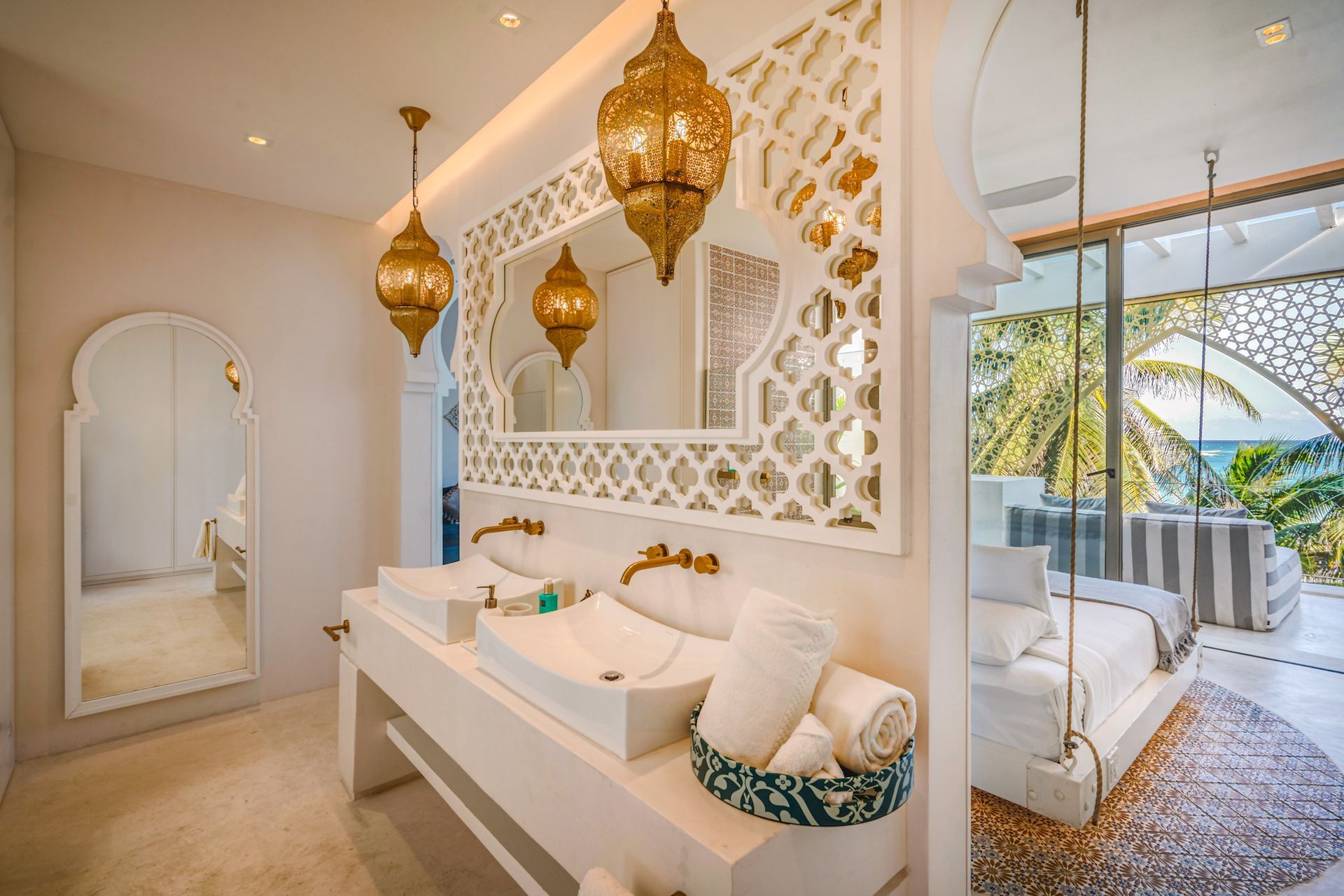 Bathroom with ornate gold lanterns, decorative wall, double sinks, and a view of the ocean.