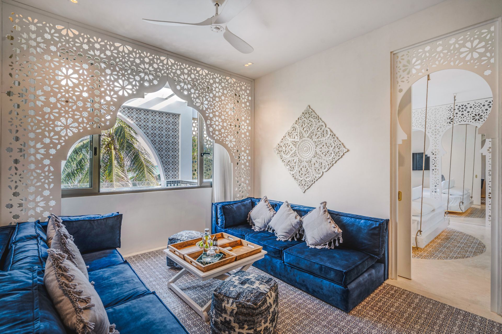 Living room with blue sofa, patterned rug, white carved screens, and a view of an outdoor building.