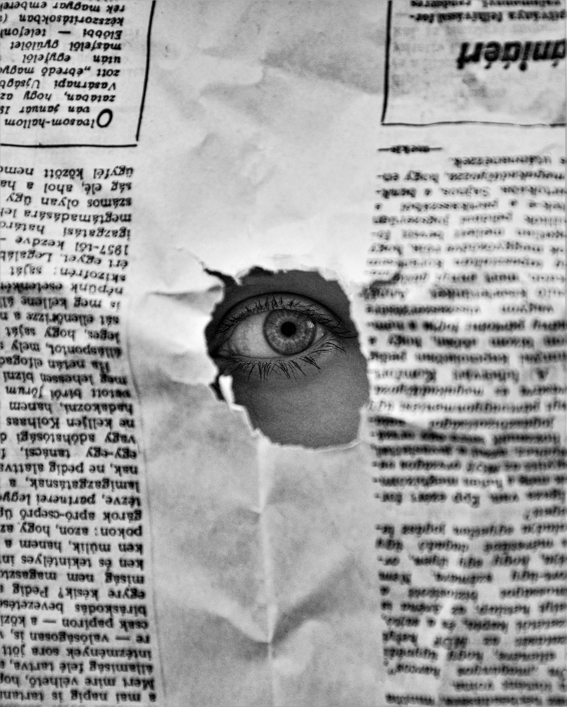 Eye peeking through a torn newspaper.