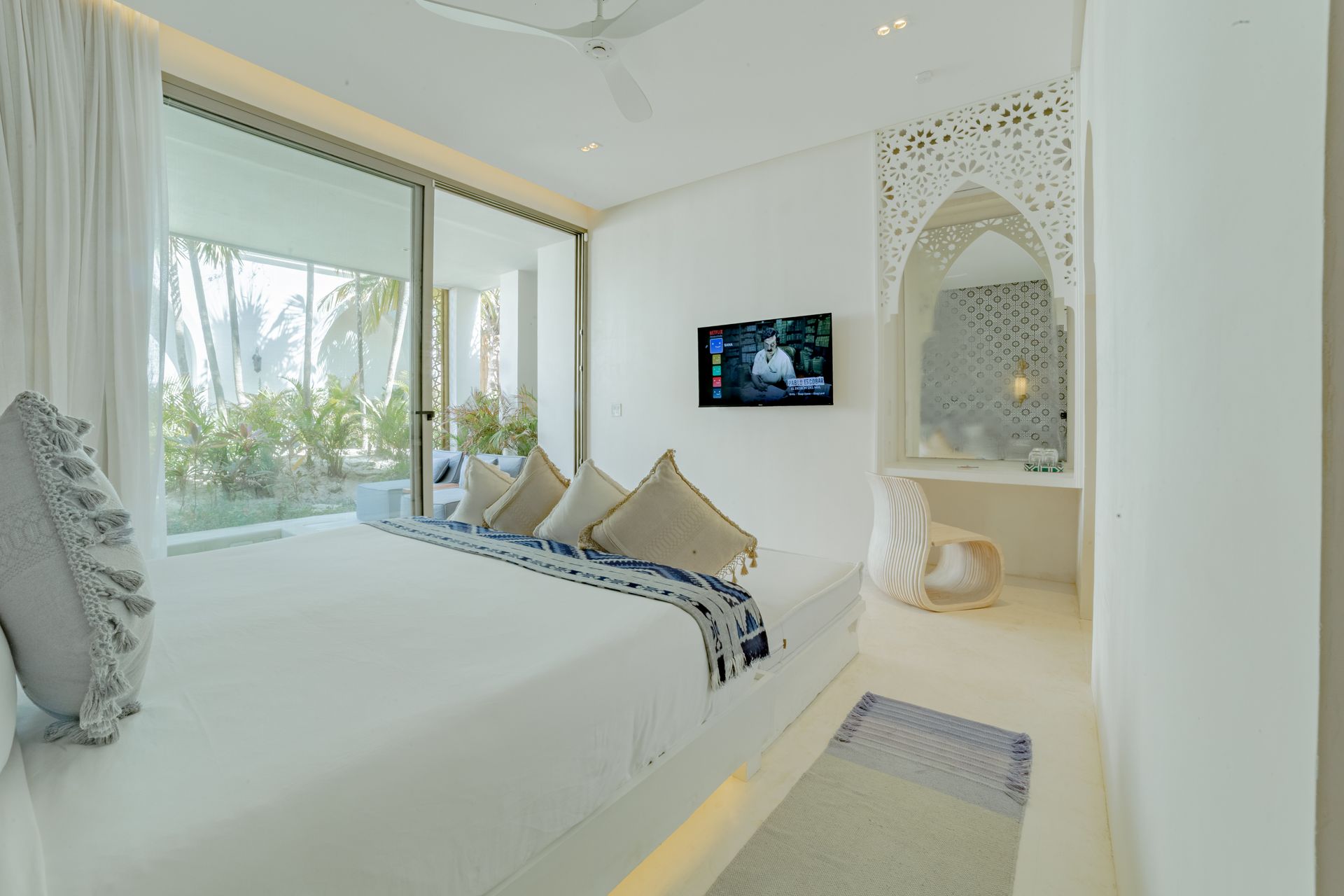 Dormitorio blanco con cama grande, puertas corredizas de vidrio, pared decorativa, TV y alfombra pequeña.