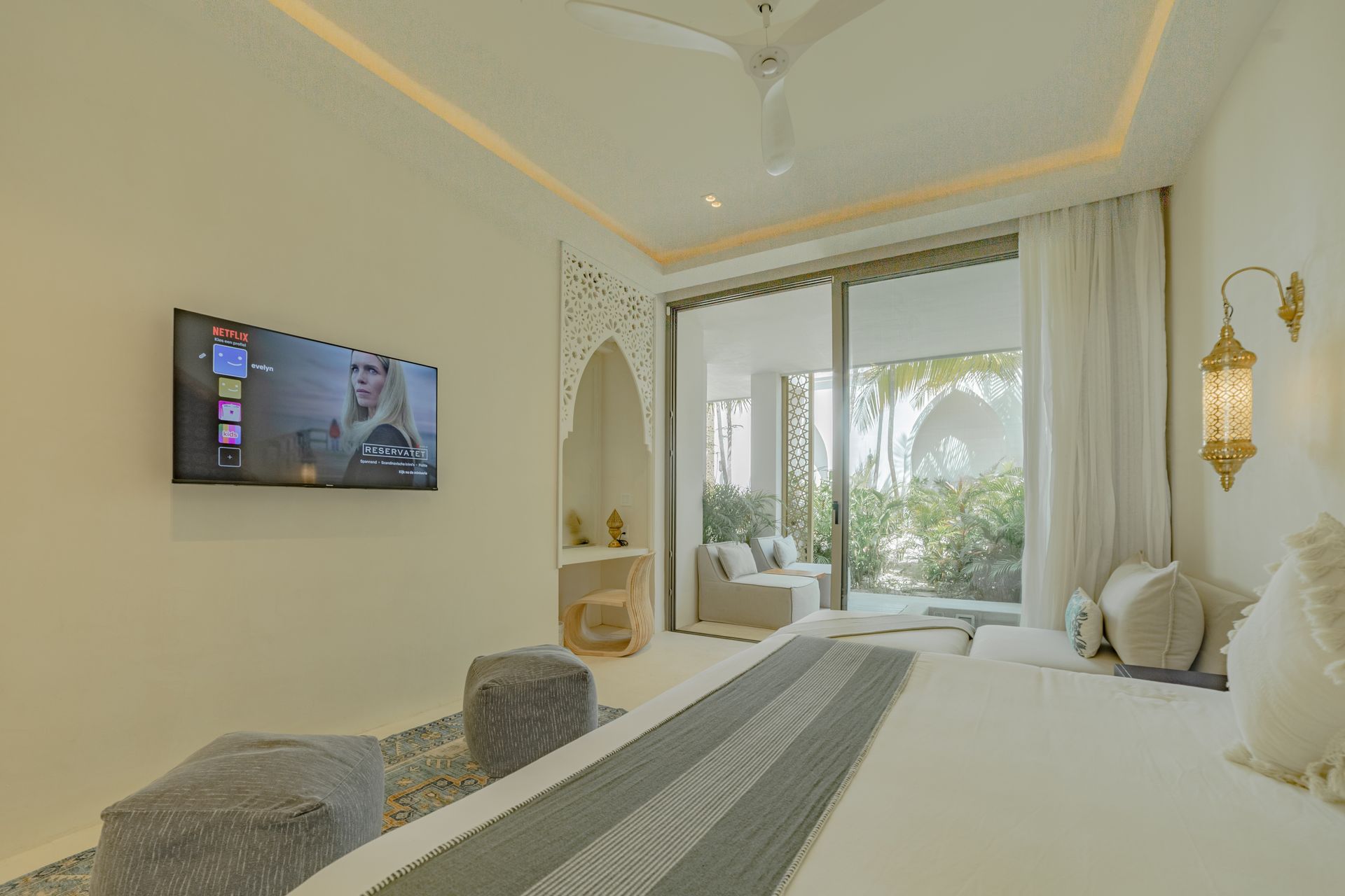 Dormitorio con paredes blancas, TV, grandes puertas corredizas a un patio e iluminación decorativa.