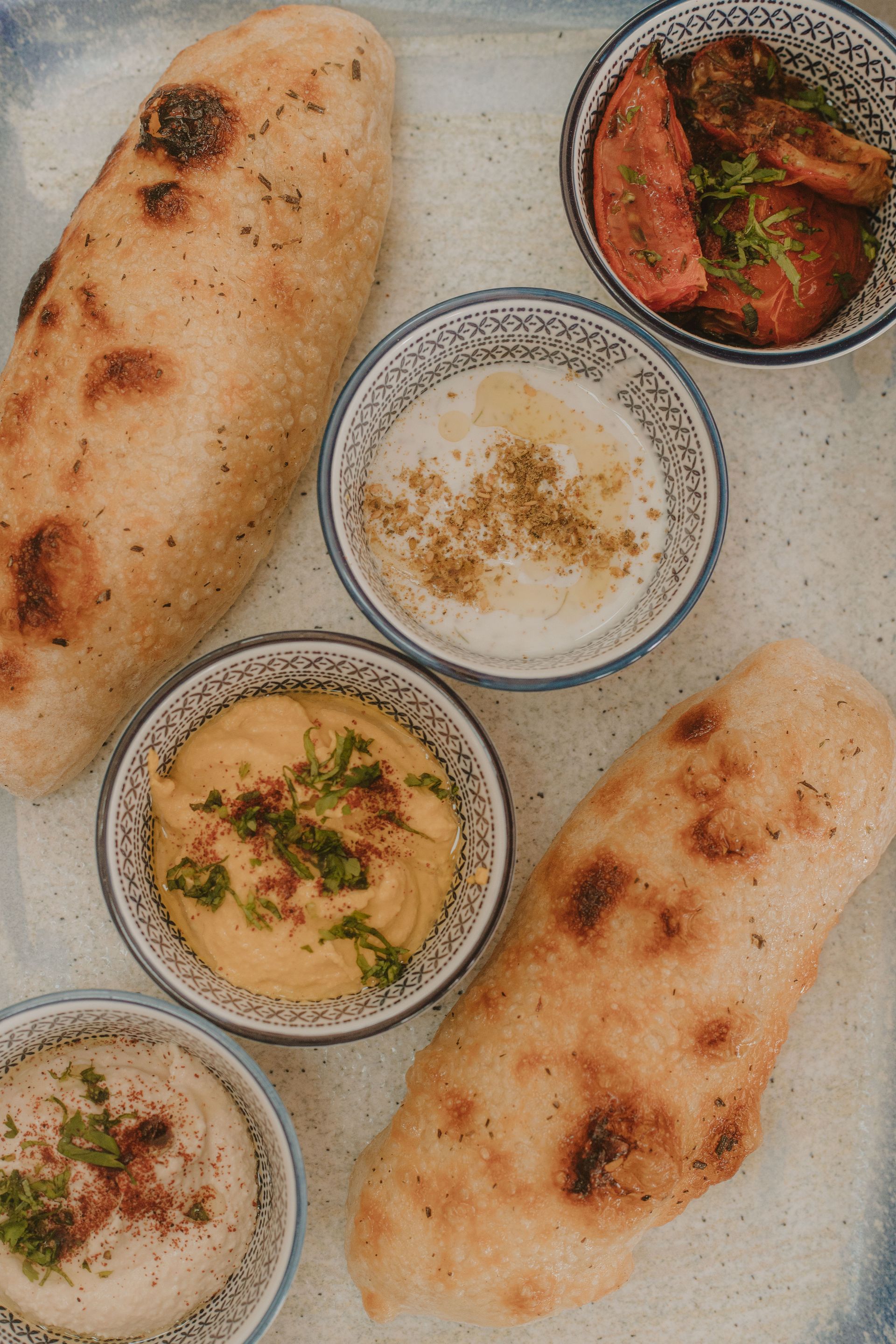 Pan plano con salsas: hummus, yogur y salsa de tomate, en una bandeja.