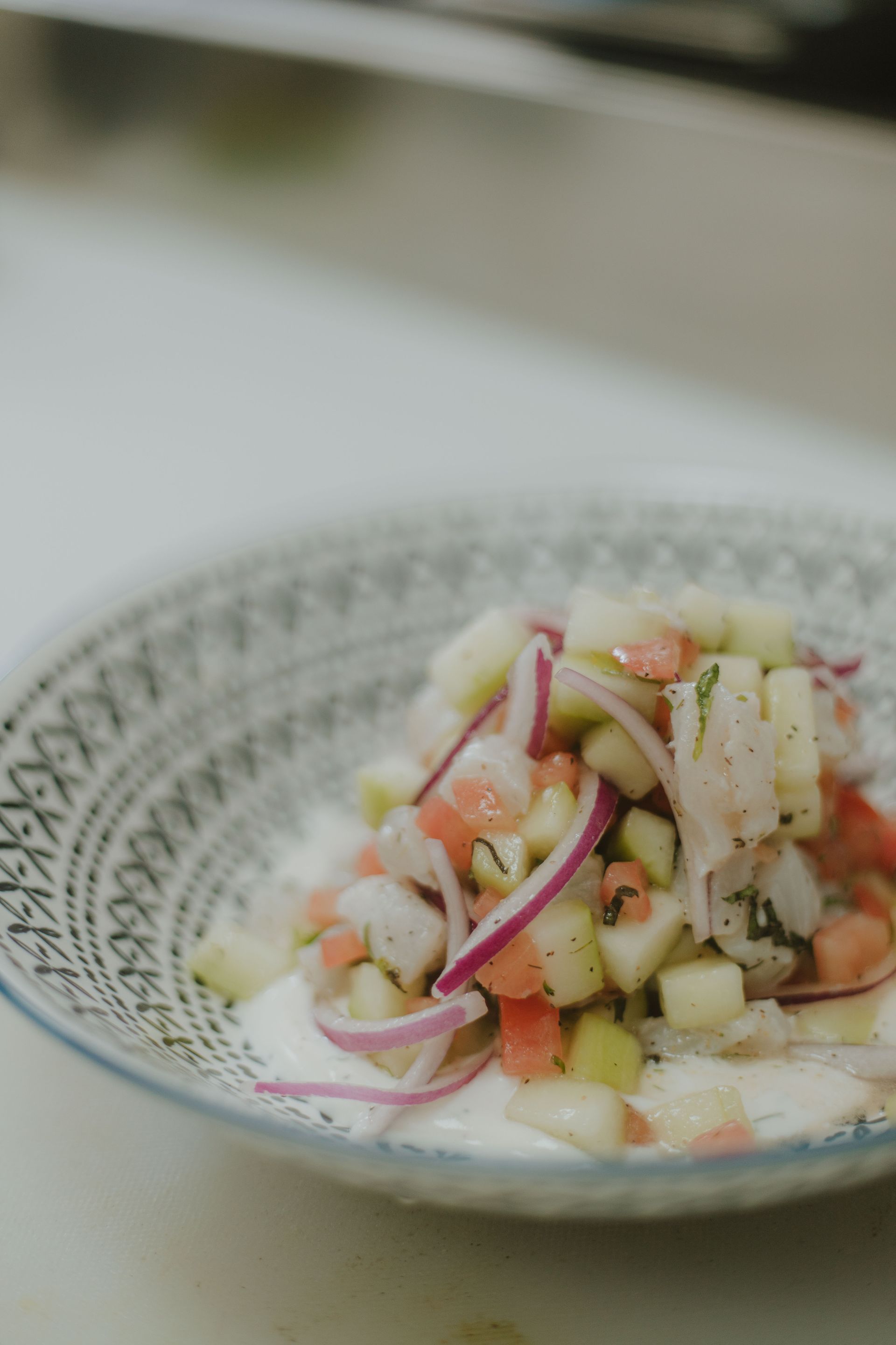 Ceviche en un recipiente estampado, con pepino cortado en cubitos, tomate y cebolla roja.