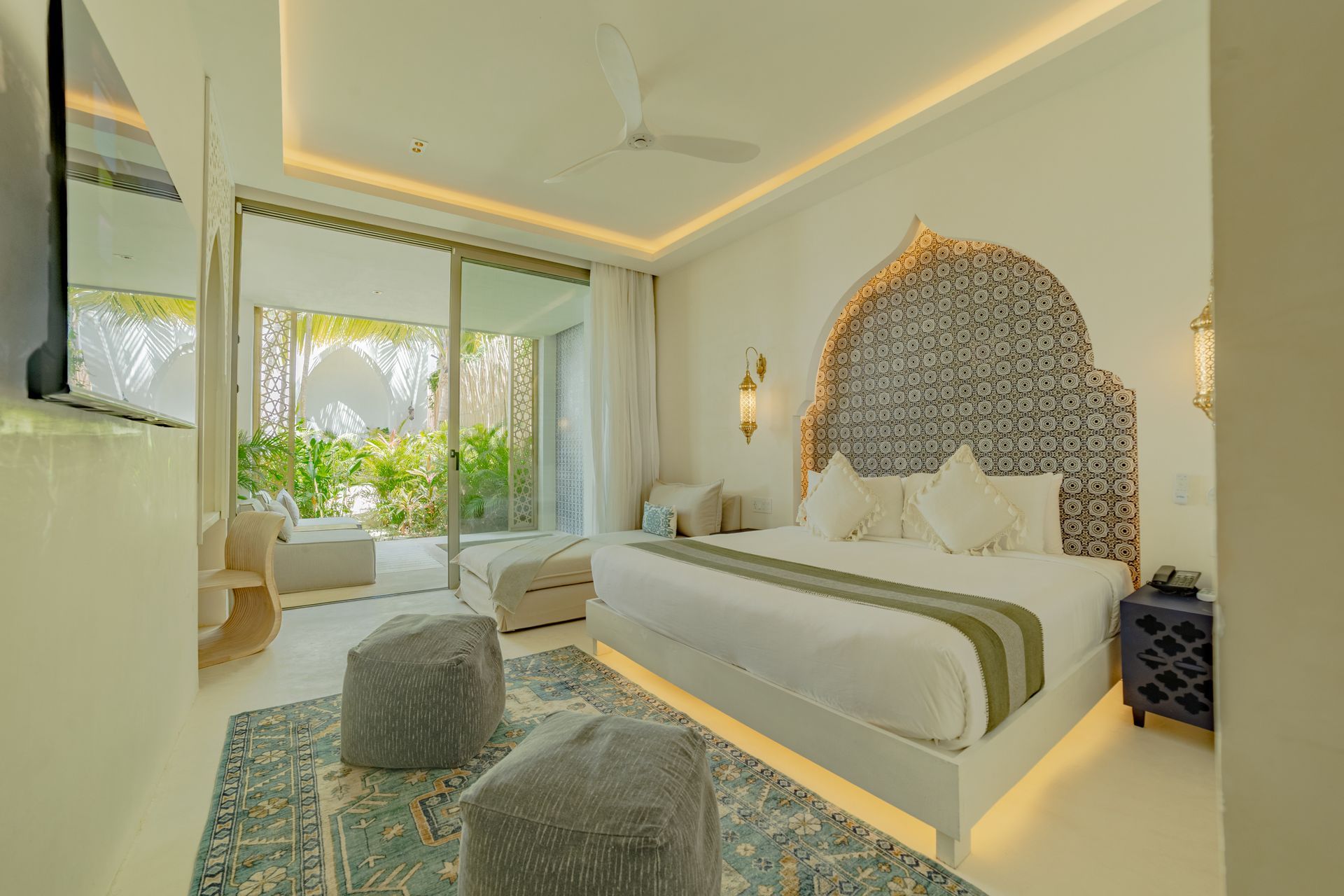 Dormitorio de lujo con cabecera ornamentada, colores claros y vista a la vegetación.