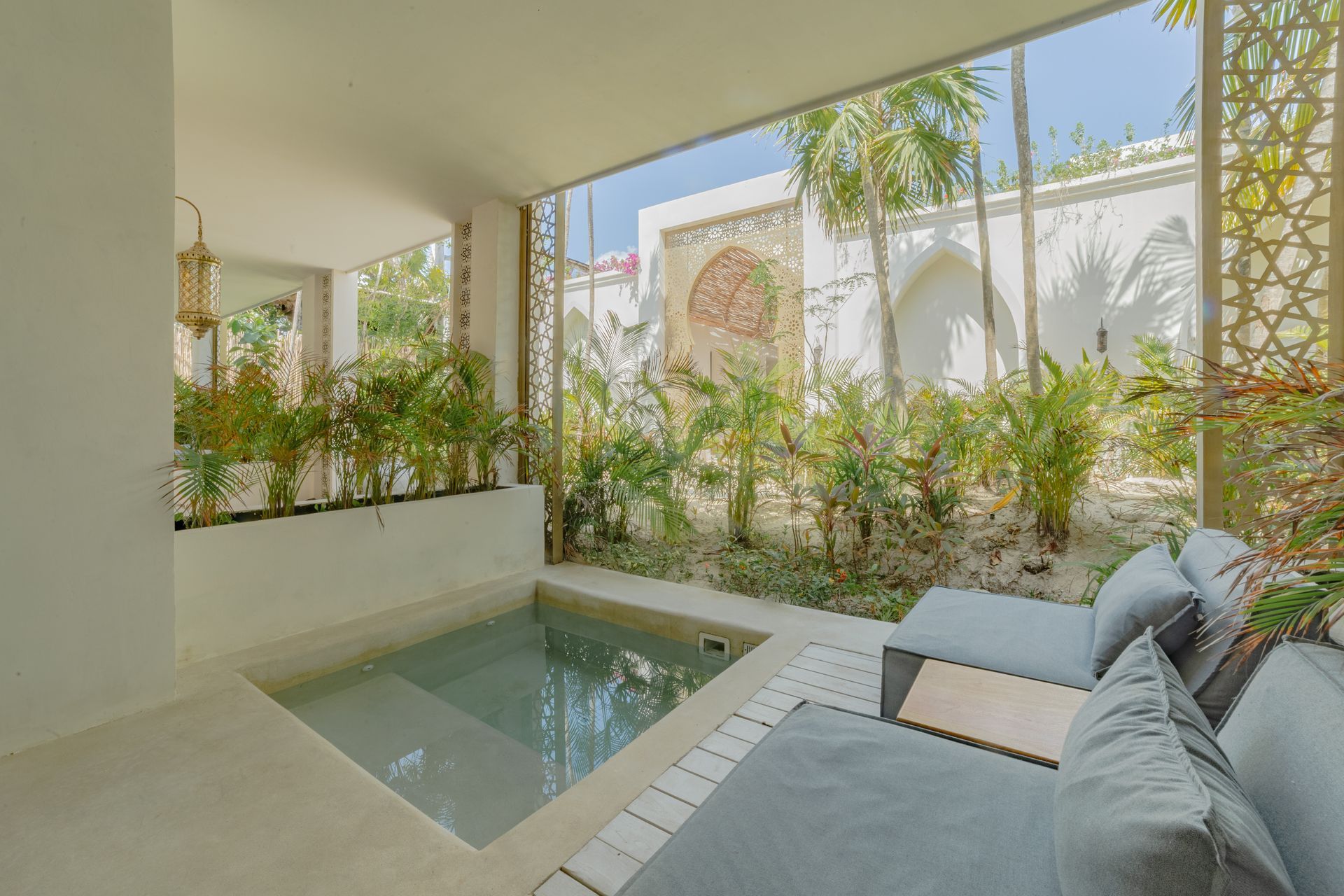 Pequeña piscina al aire libre y zona de estar con plantas tropicales y detalles arquitectónicos ornamentados.