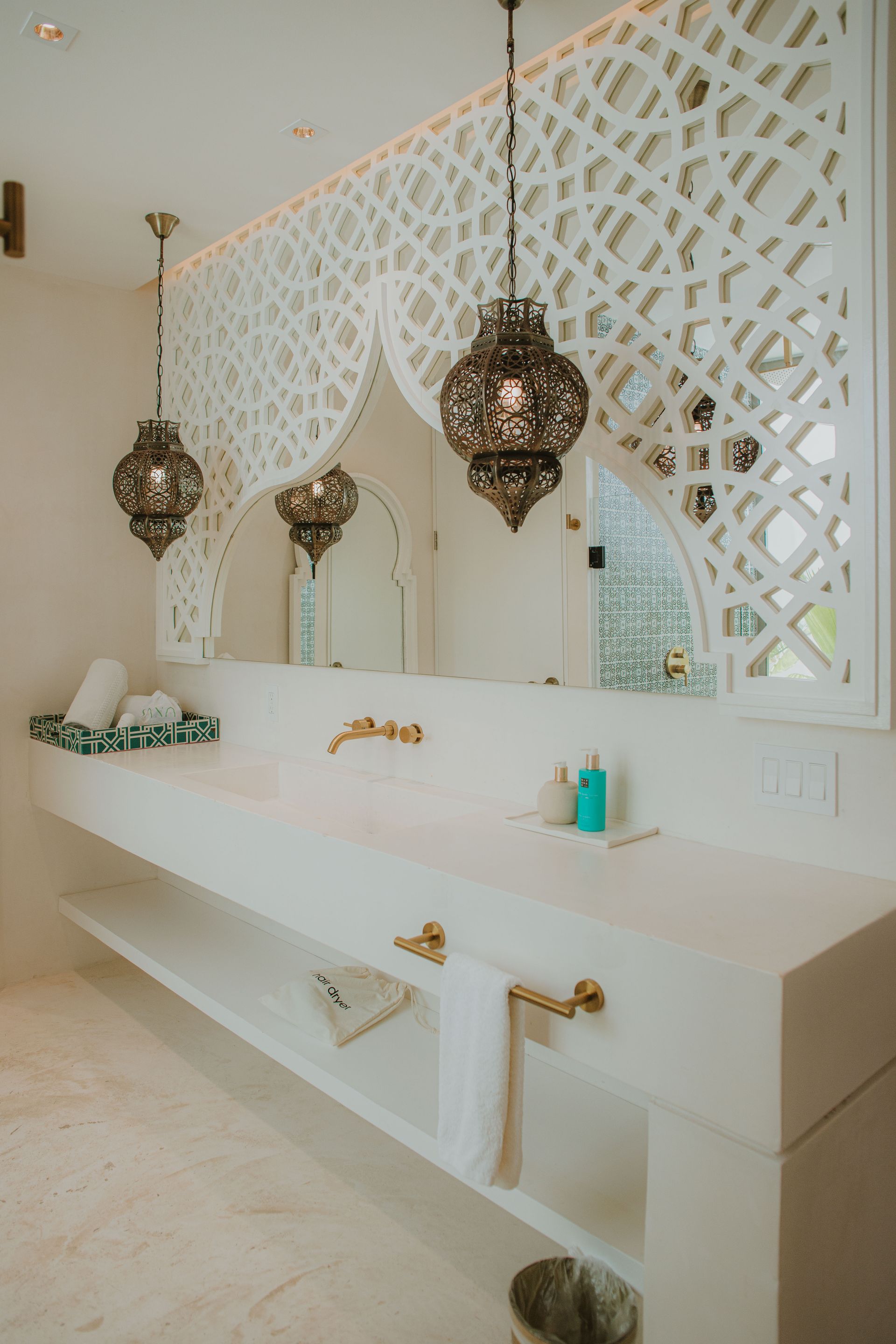 Baño con artefactos de iluminación ornamentados, panel de pared blanco tallado, espejo grande y accesorios dorados.