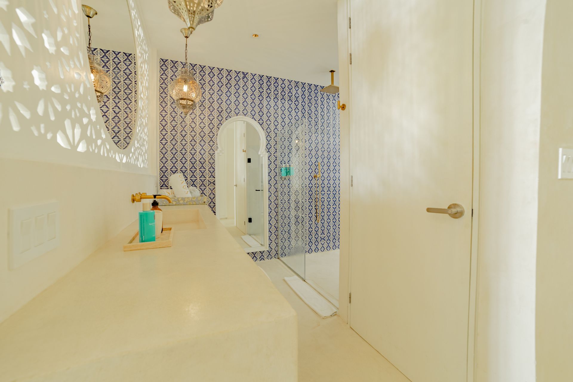 Baño con pared de azulejos azules, arco, paredes blancas e iluminación ornamentada.