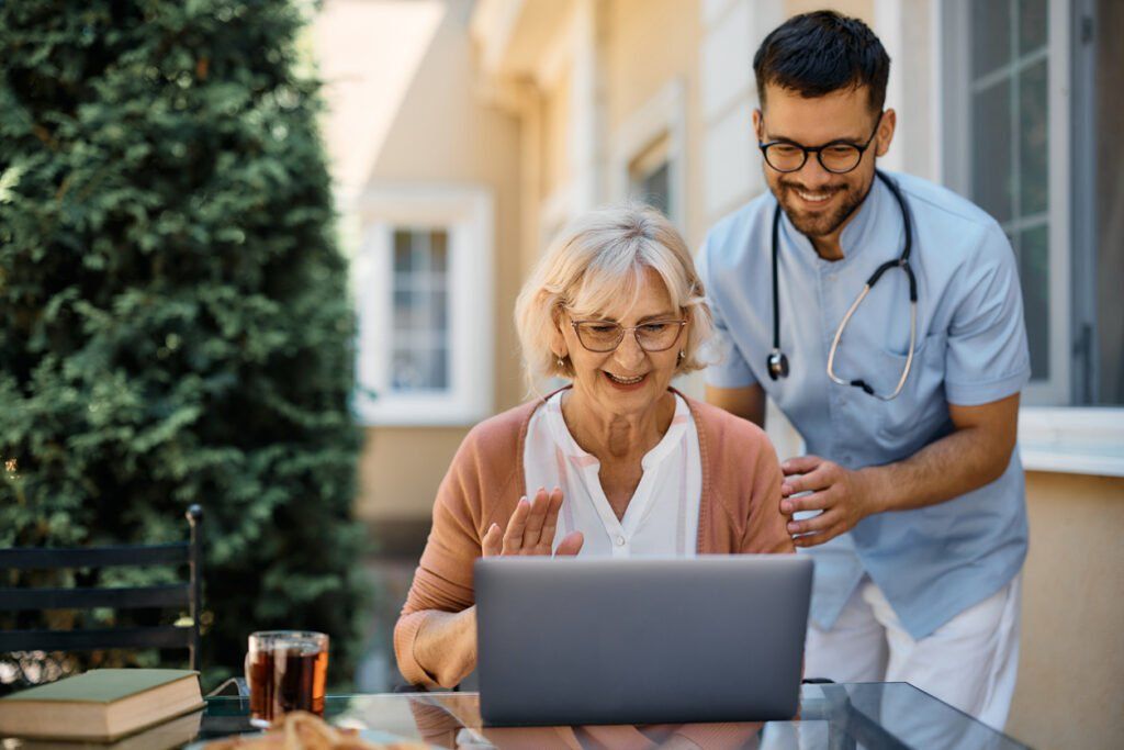 Caretaker helping elderly woman video chat on a laptop